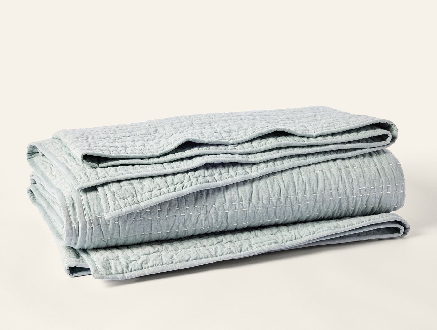 Close-up of folded Coyuchi Channel Handstitched quilt in pale sage with textured stitching.