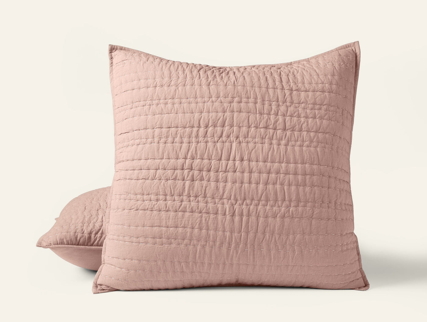 Blush pink quilted pillow shams with channel hand-stitching, stacked pair on white background.