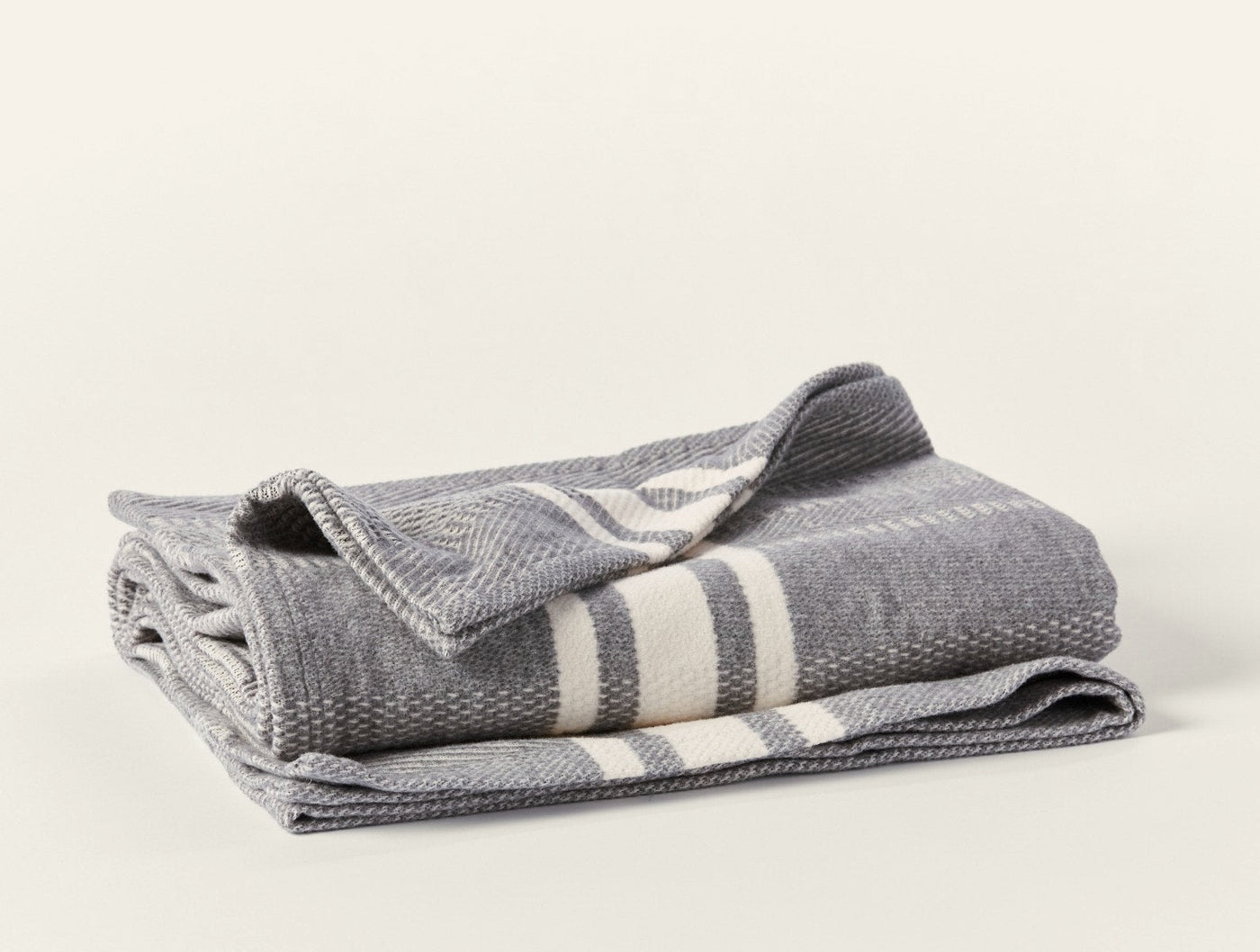 Ivory stripe detail on folded grey Coyuchi Cirrus Supersoft throw, herringbone weave visible.