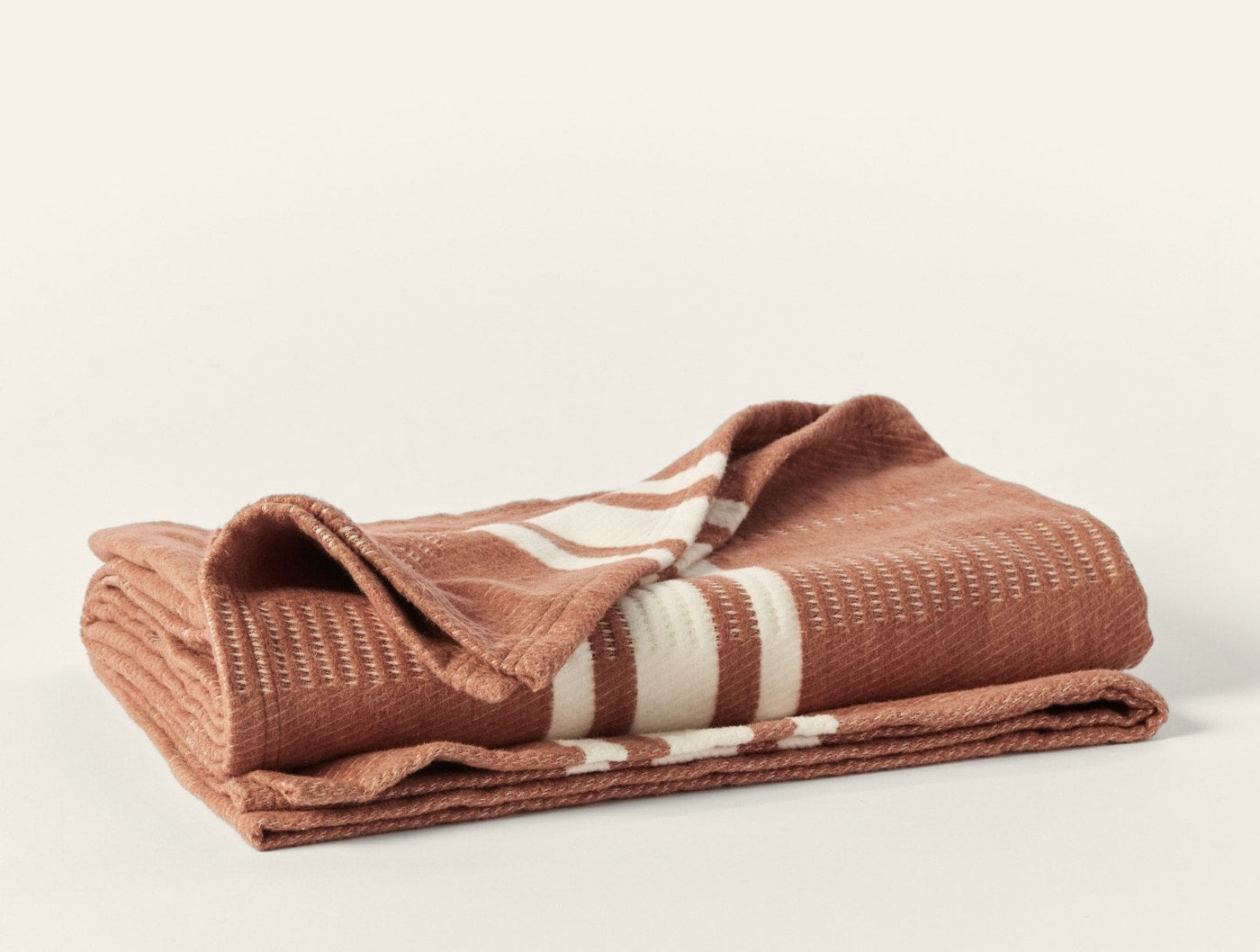 Close-up of folded terracotta Coyuchi Cirrus Supersoft throw showing ivory stripe detail and waffle texture.