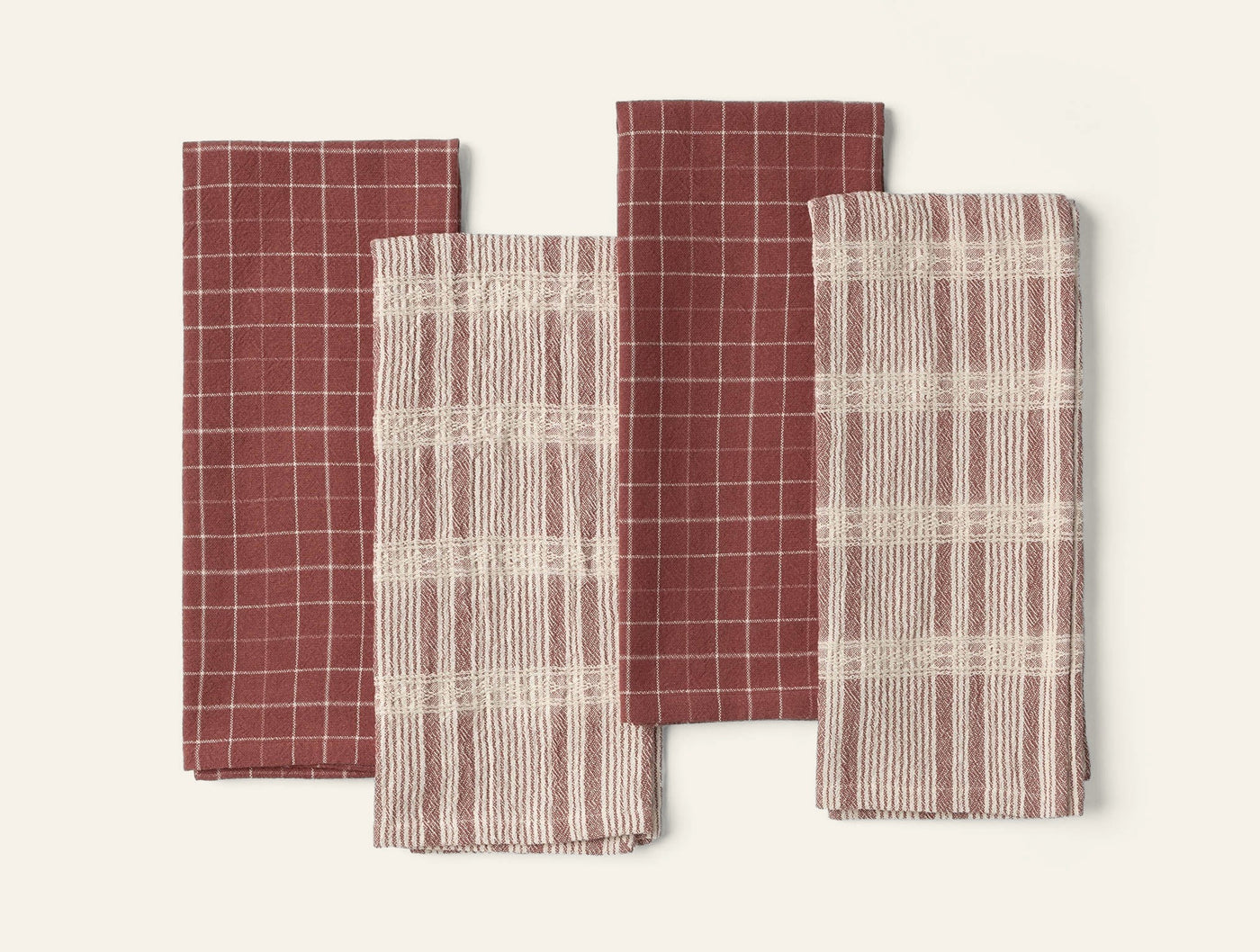 Coyuchi Clarendon kitchen towels in crimson, four folded showing grid and plaid weave patterns.