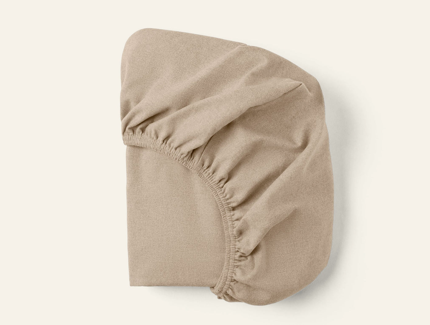 Underside view of a sand fitted sheet showing elasticized corners and hem detail.