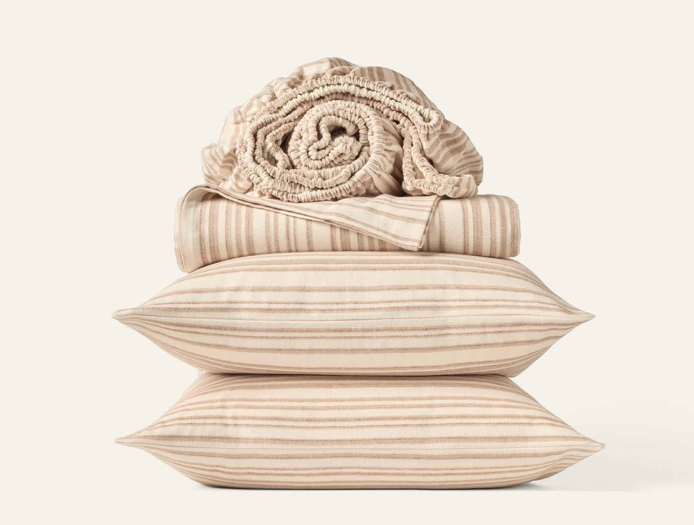 Close-up of stacked Coyuchi flannel pillowcases and rolled blanket in warm stripe pattern.