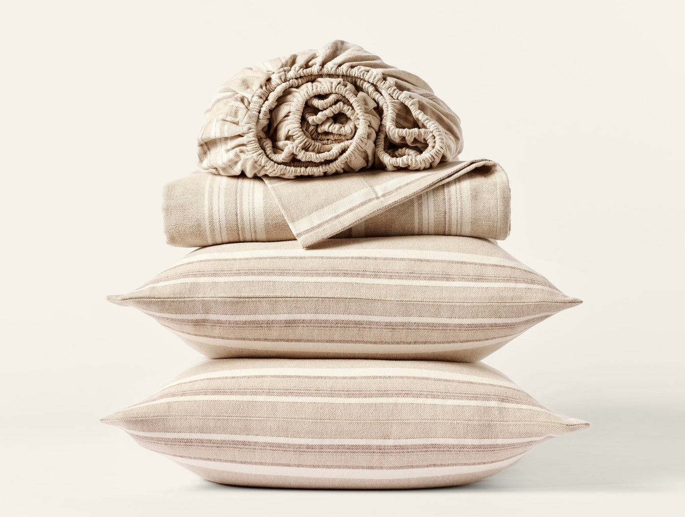 Close-up of stacked oatmeal stripe flannel pillowcases and folded sheets on white background.