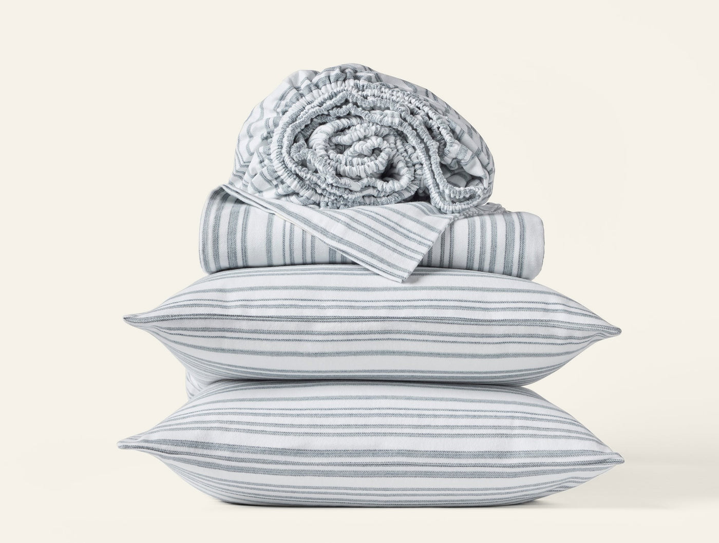 Close-up of stacked Coyuchi Cloud Brushed Flannel pillowcases in grey stripe with folded sheets.