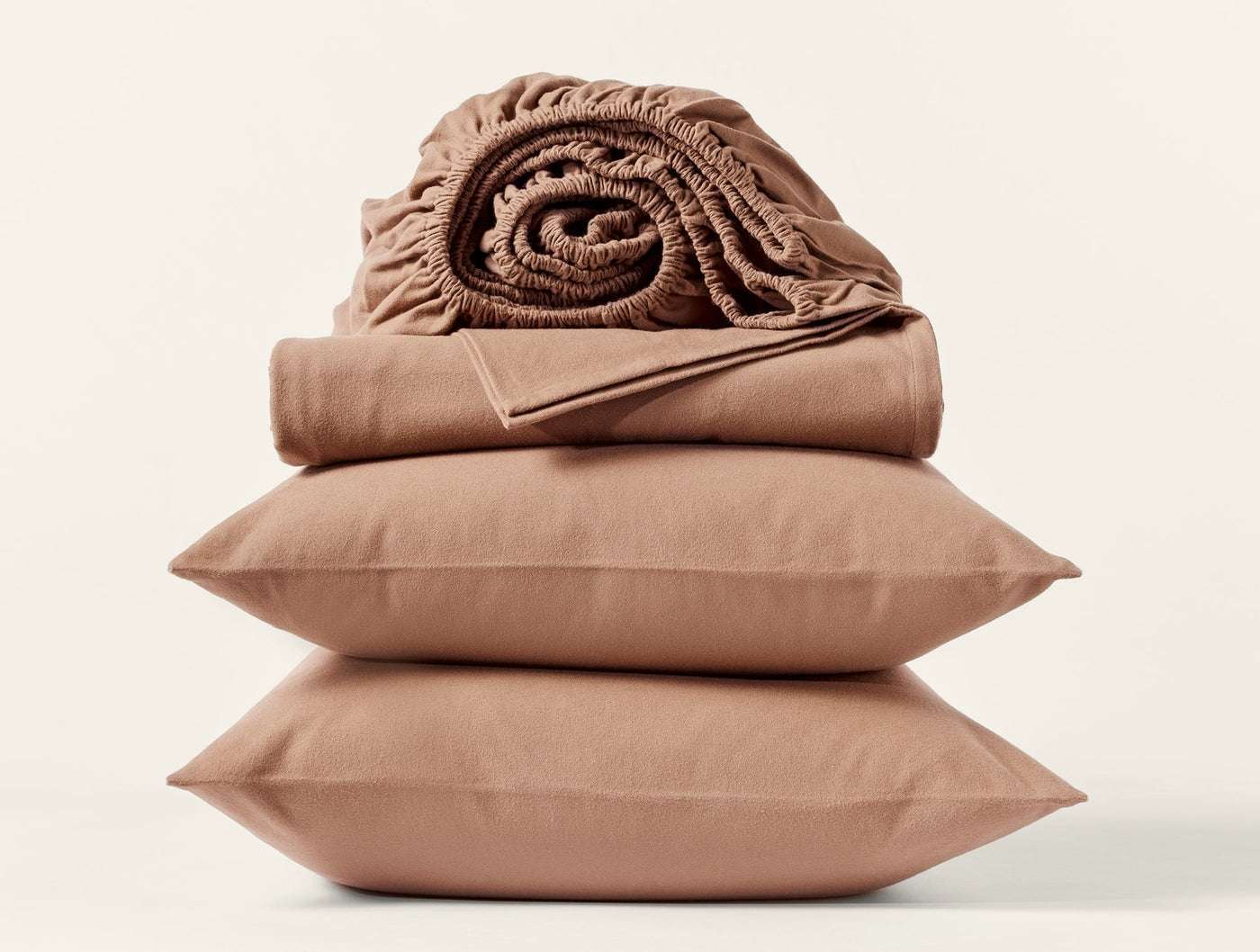 Close-up of stacked caramel Coyuchi flannel pillowcases with folded and rolled sheets on top.