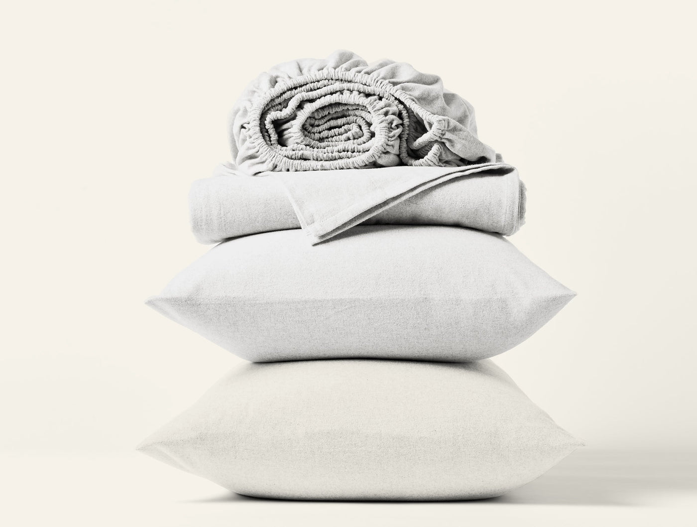 Coyuchi Cloud Brushed Flannel sheet set in white, stacked with pillows and folded sheets.