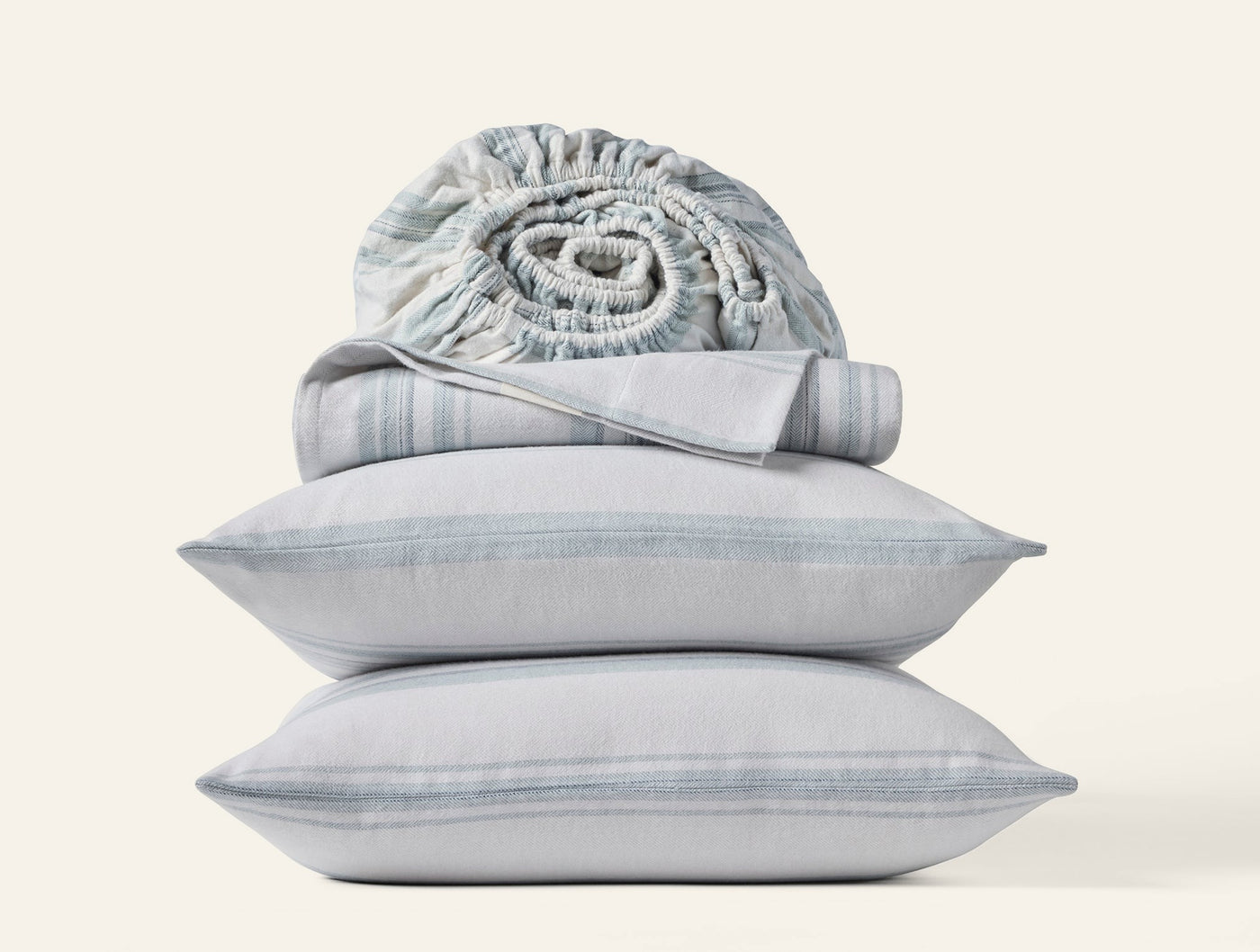 Two stacked Coyuchi Cloud Brushed Flannel pillowcases with blue stripe, rolled fitted sheet on top.