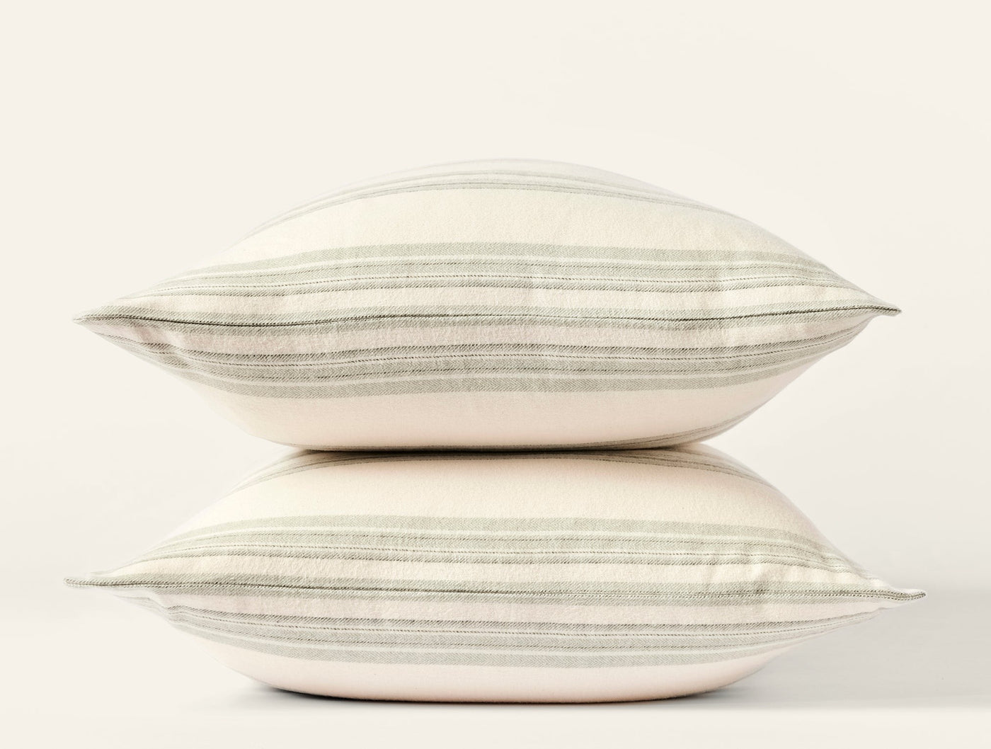 Close-up side view of two stacked ivory pillows with sage and grey horizontal stripes.