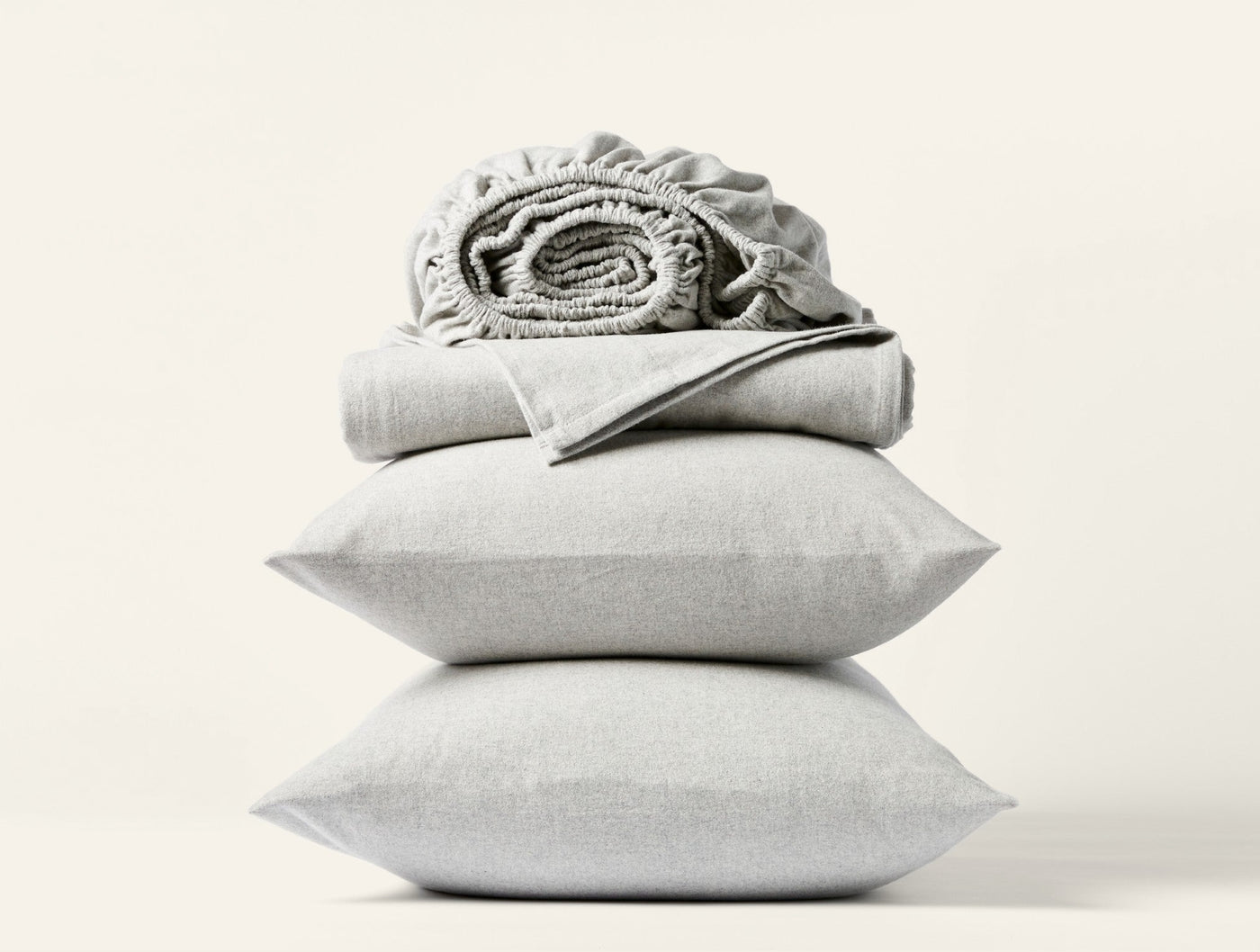 Stacked sage Coyuchi Cloud Brushed Flannel pillowcases with rolled fitted sheet on top.