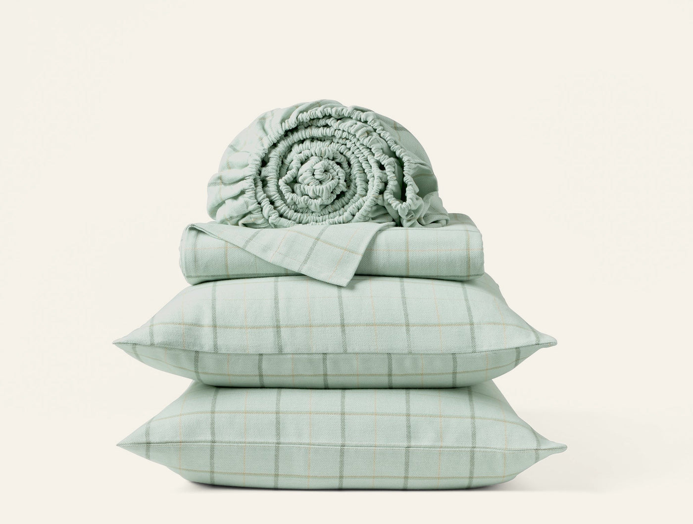 Close-up of sage green plaid flannel sheet set stacked with rolled blanket and two pillowcases.
