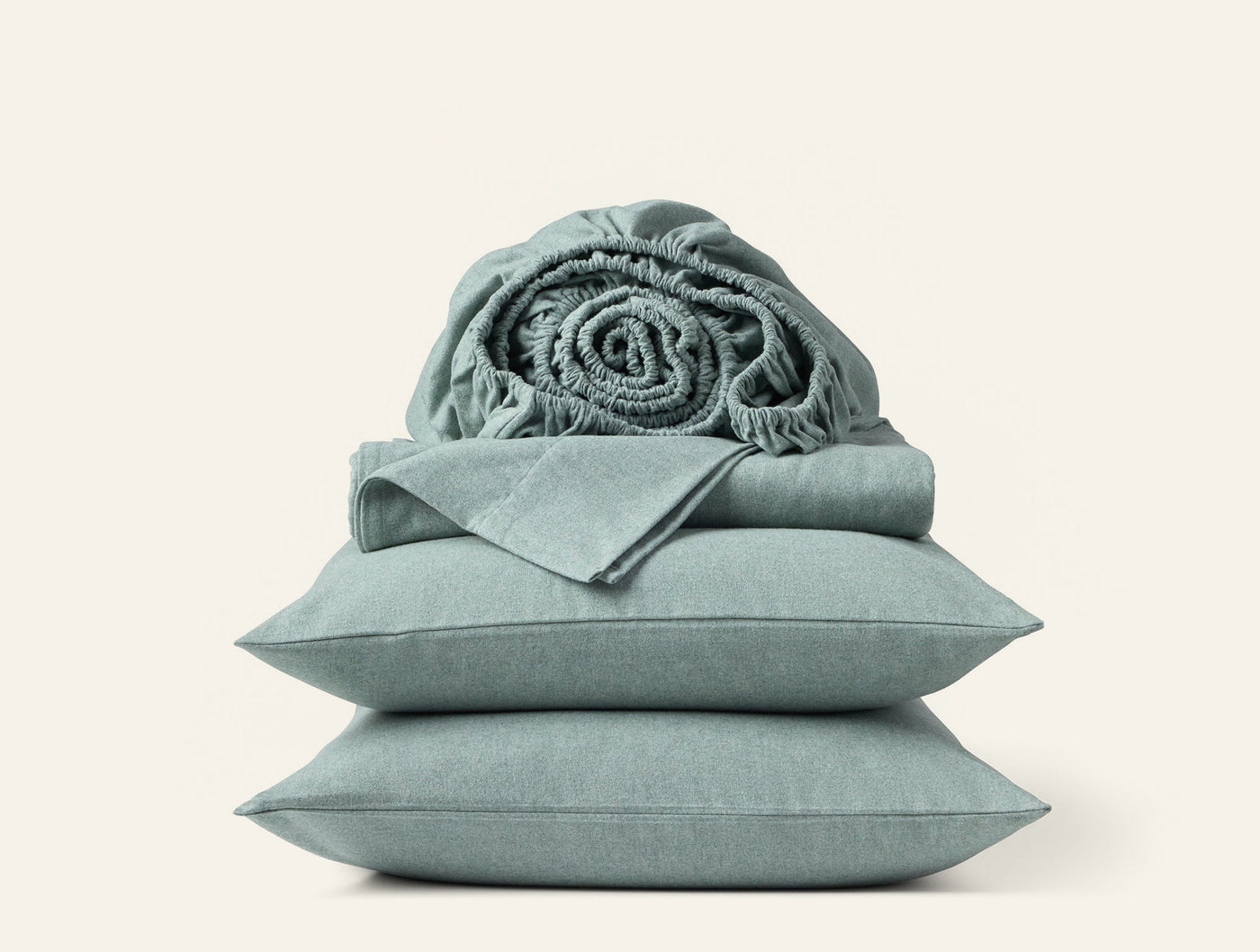 Rolled flannel throw resting atop folded sage green sheets and stacked pillowcases.