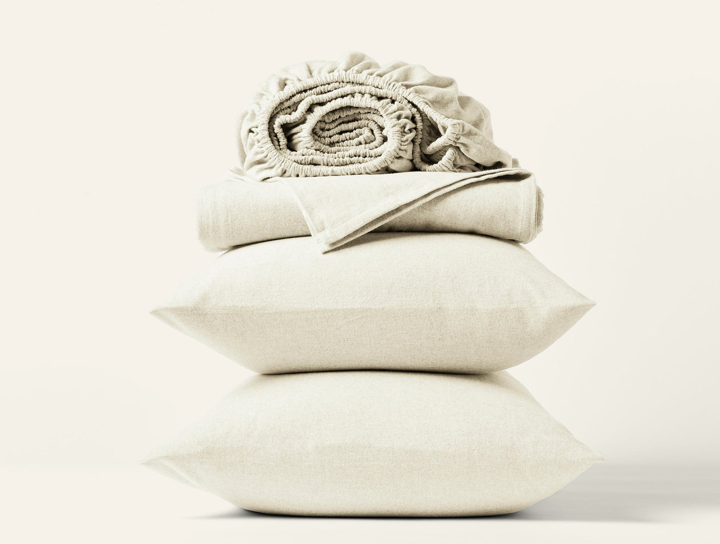 Stacked ivory flannel pillow shams and folded sheets with a ruffled fitted sheet on top.