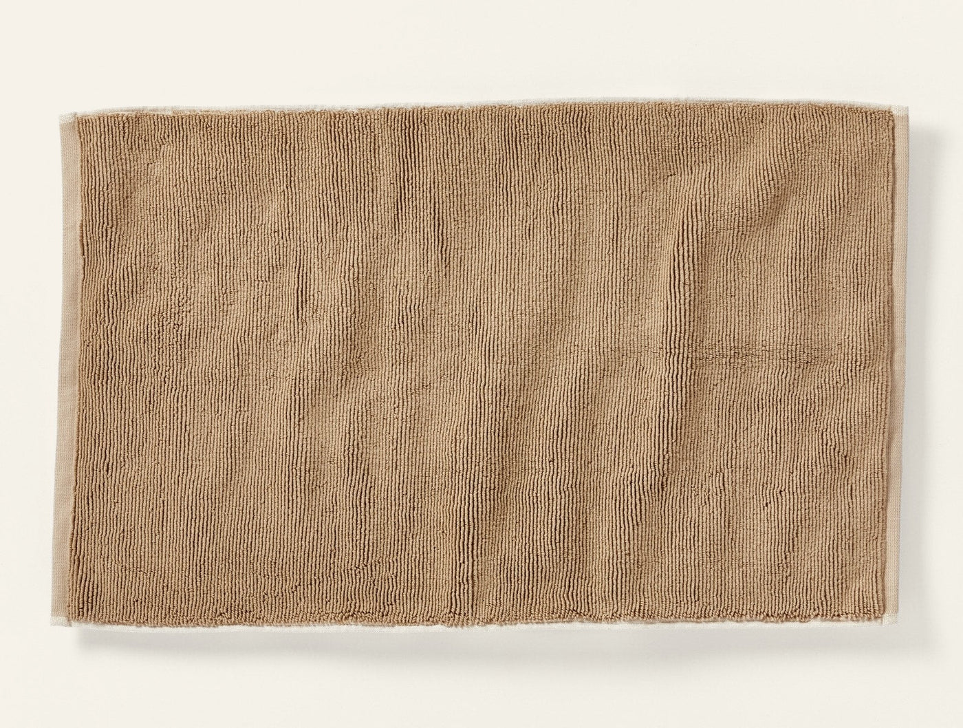 Coyuchi Cloud Loom bath rug in warm tan, flat lay showing textured cotton pile surface.