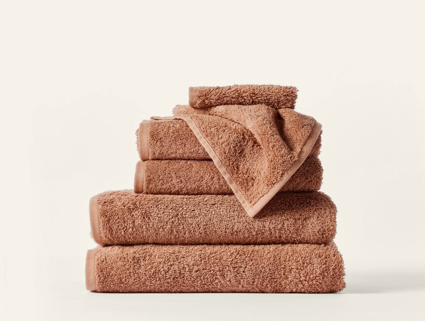 Stacked Coyuchi Cloud Loom towels in terracotta, showing varied sizes from washcloth to bath sheet.