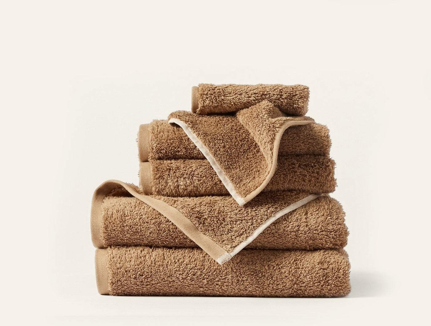 Stack of caramel Coyuchi Cloud Loom towels in varied sizes with ivory border trim.