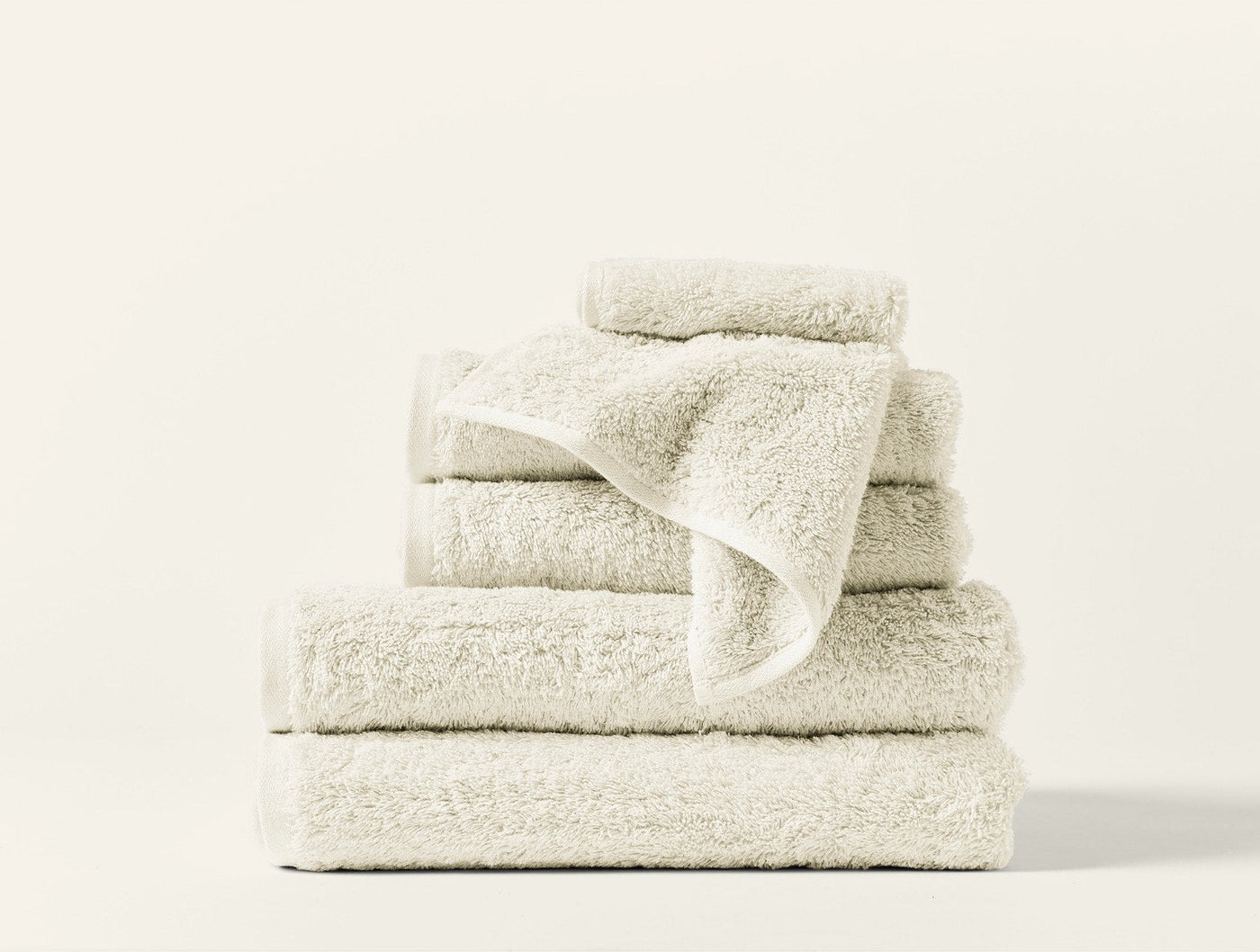 Stacked ivory Coyuchi Cloud Loom towels in assorted sizes against white background.