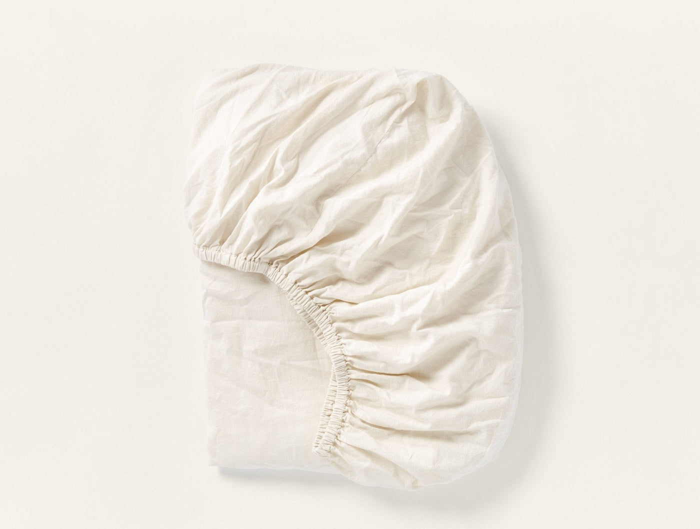 Ivory fitted sheet gathered at corners, showing elastic hem detail and soft sateen fabric texture.