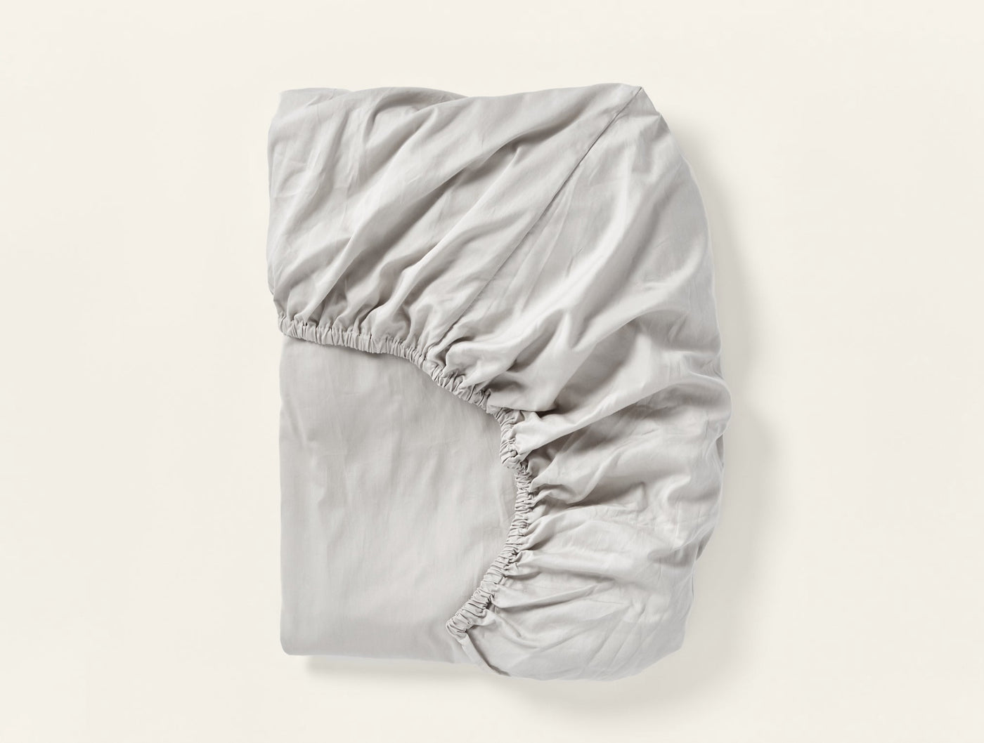 Coyuchi Cloud Soft Sateen fitted sheet folded, silver grey, elasticated corners visible.
