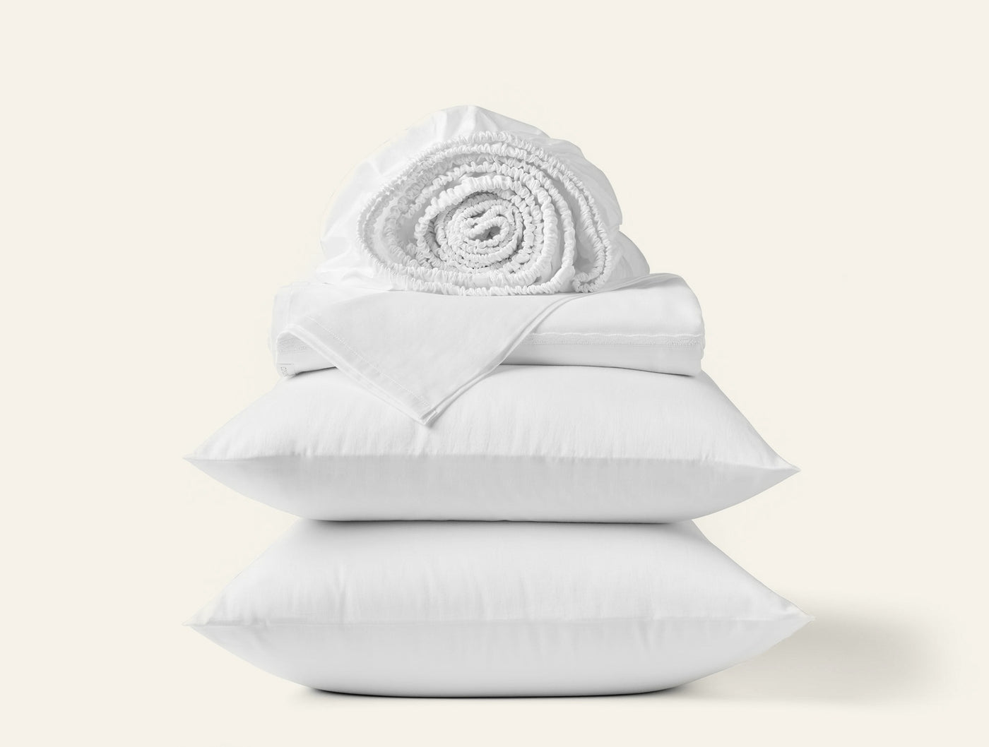 Stacked white Coyuchi Cloud Soft Sateen sheet set with rolled blanket atop two pillows.