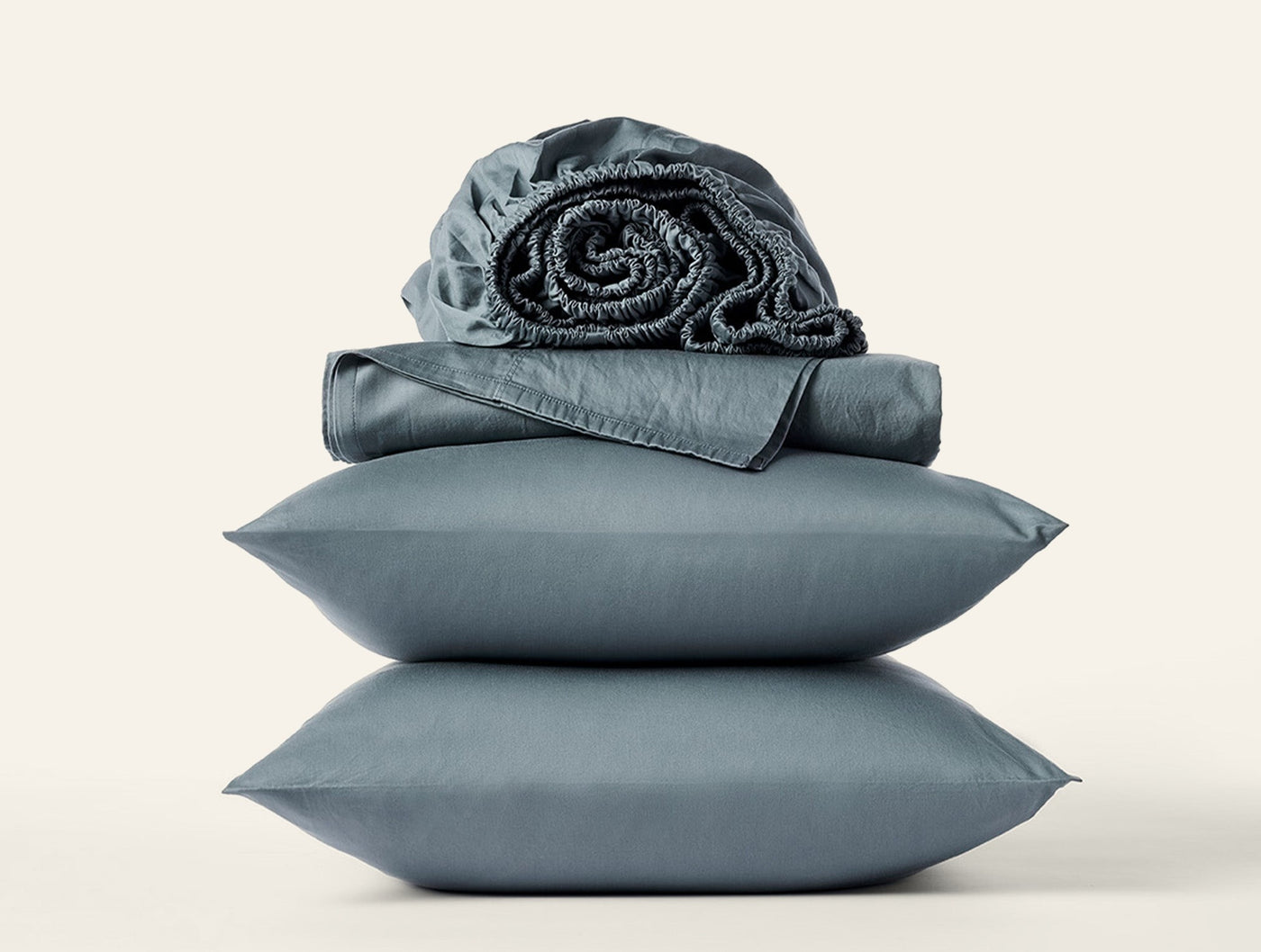 Close-up of stacked slate Coyuchi Cloud Soft Sateen pillowcases with folded and rolled sheets.