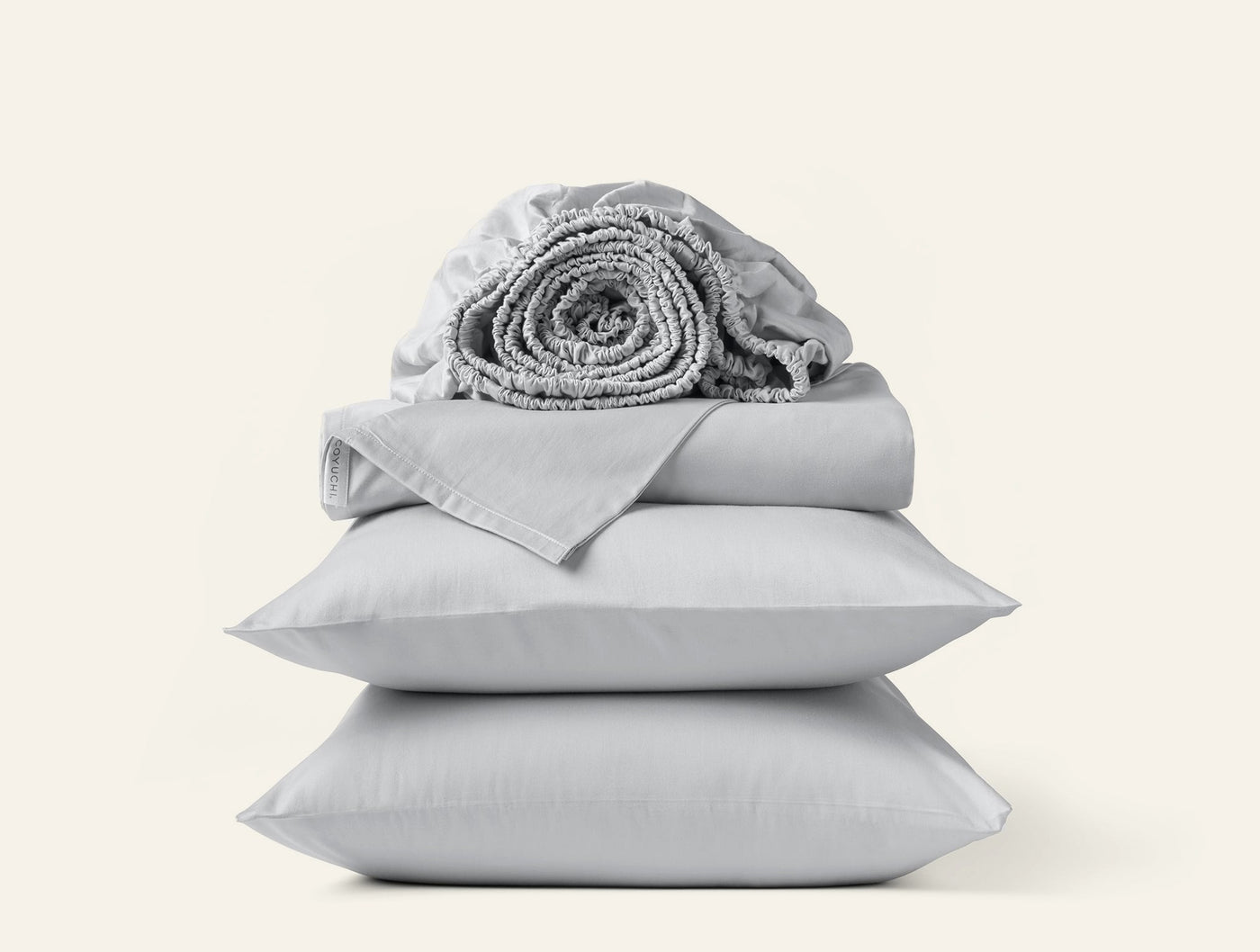Stacked silver grey sateen sheet set with rolled fitted sheet atop folded flat sheet and two pillowcases.