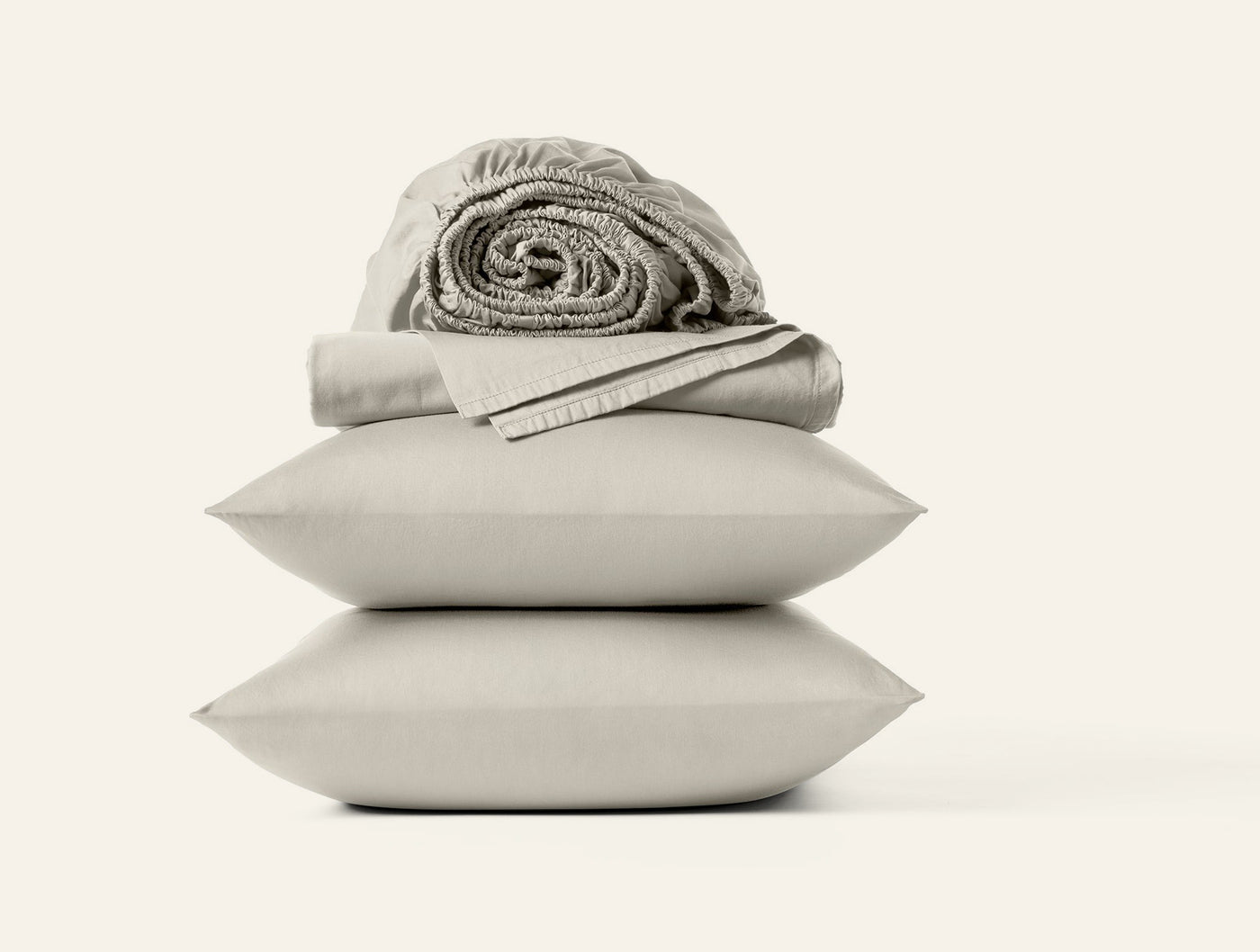 Close-up of stacked sand Coyuchi Cloud Soft Sateen pillowcases with rolled fitted sheet on top.