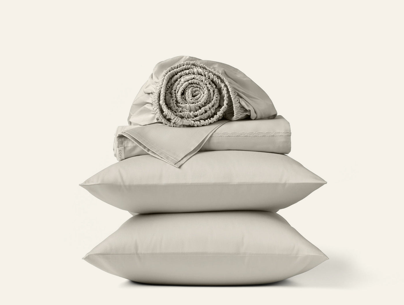 Stacked Coyuchi pillowcases in pebble with rolled sateen sheet set on top.