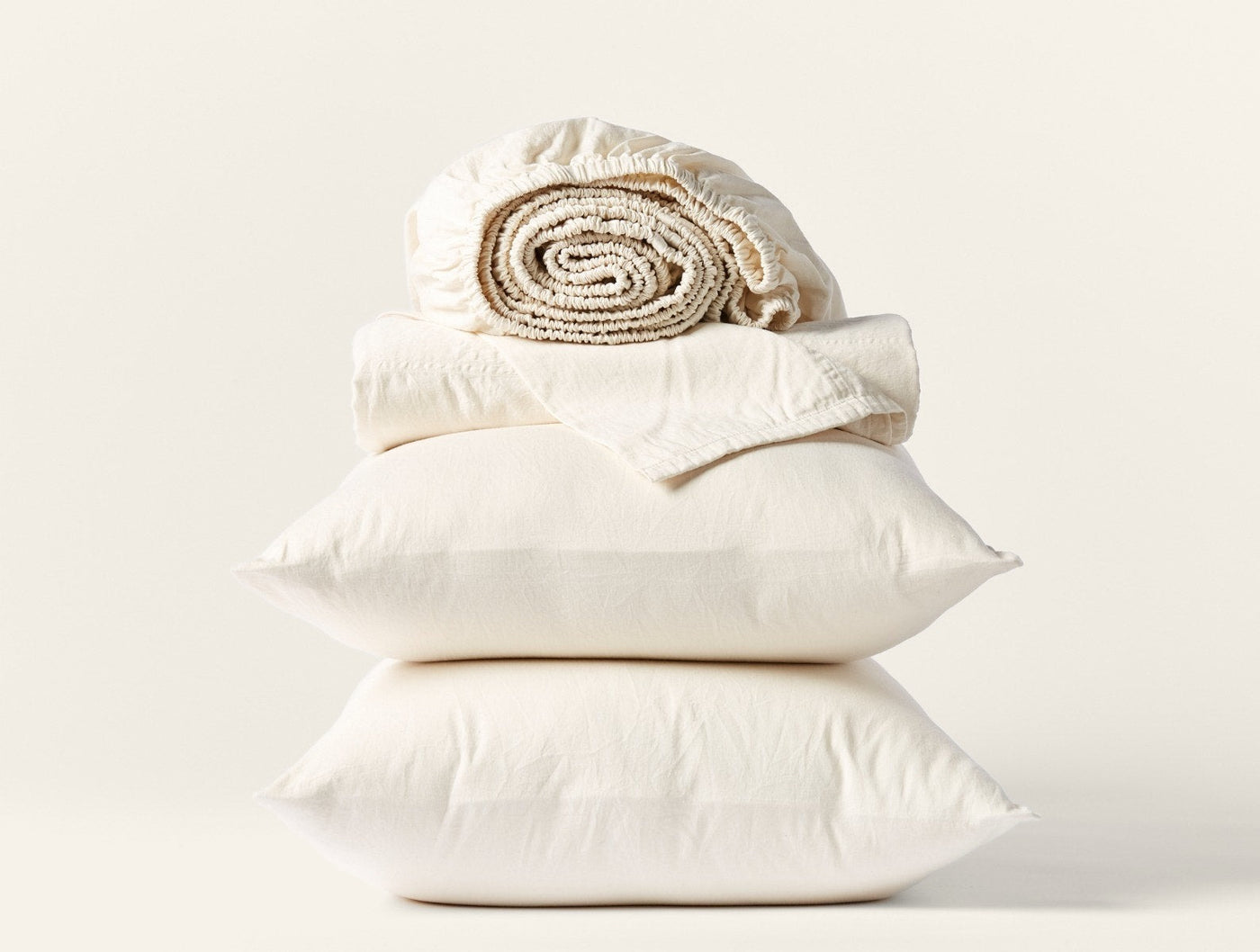 Ivory sateen sheet set stacked with two pillowcases and a rolled fitted sheet.