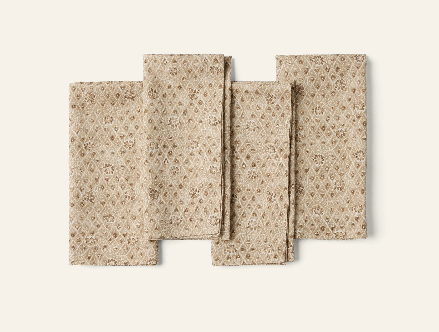 Close-up of four folded Coyuchi Coral Bell Print napkins in tan with floral diamond pattern.