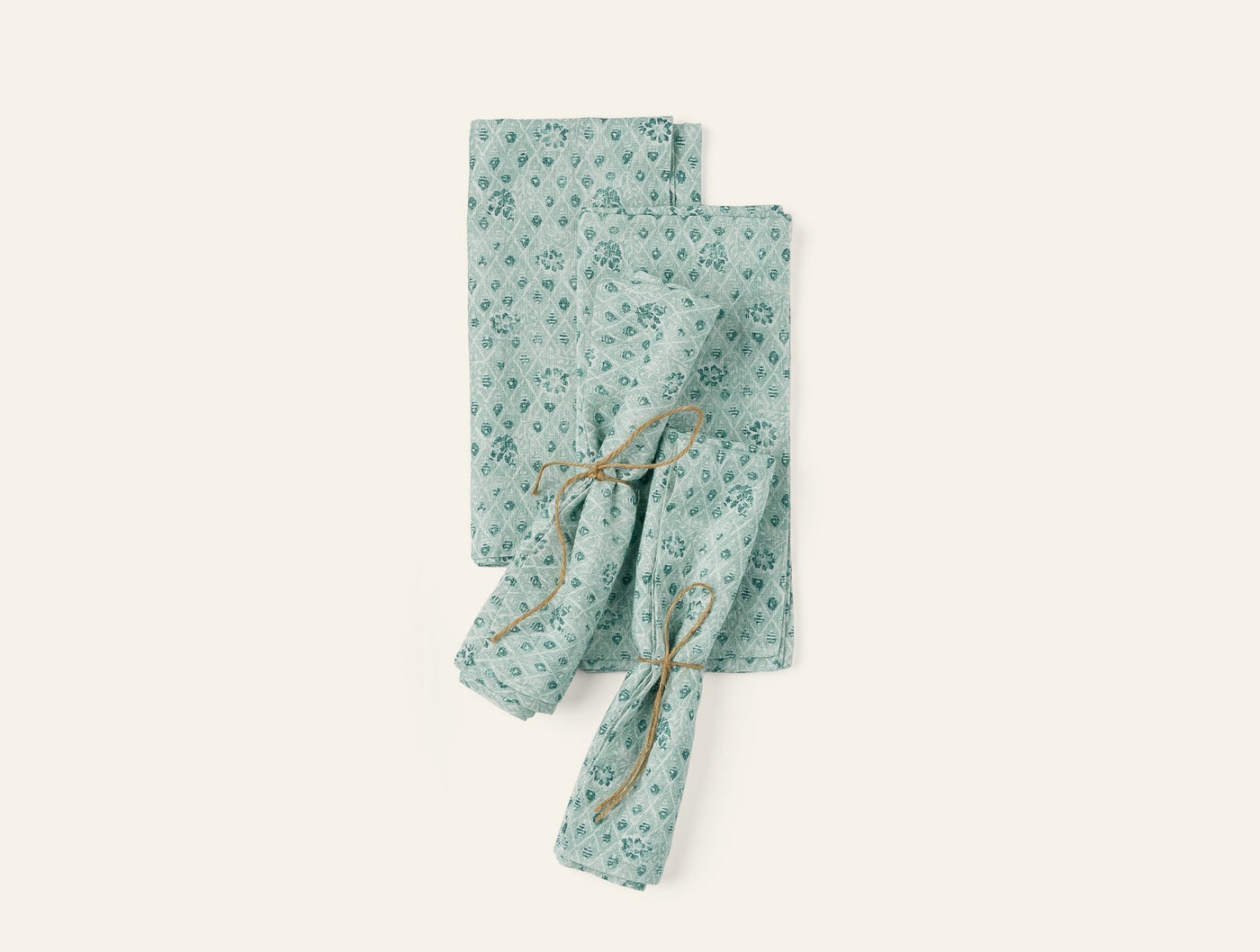 Coyuchi Coral Bell Print napkins in sage green, two folded and one tied with twine.