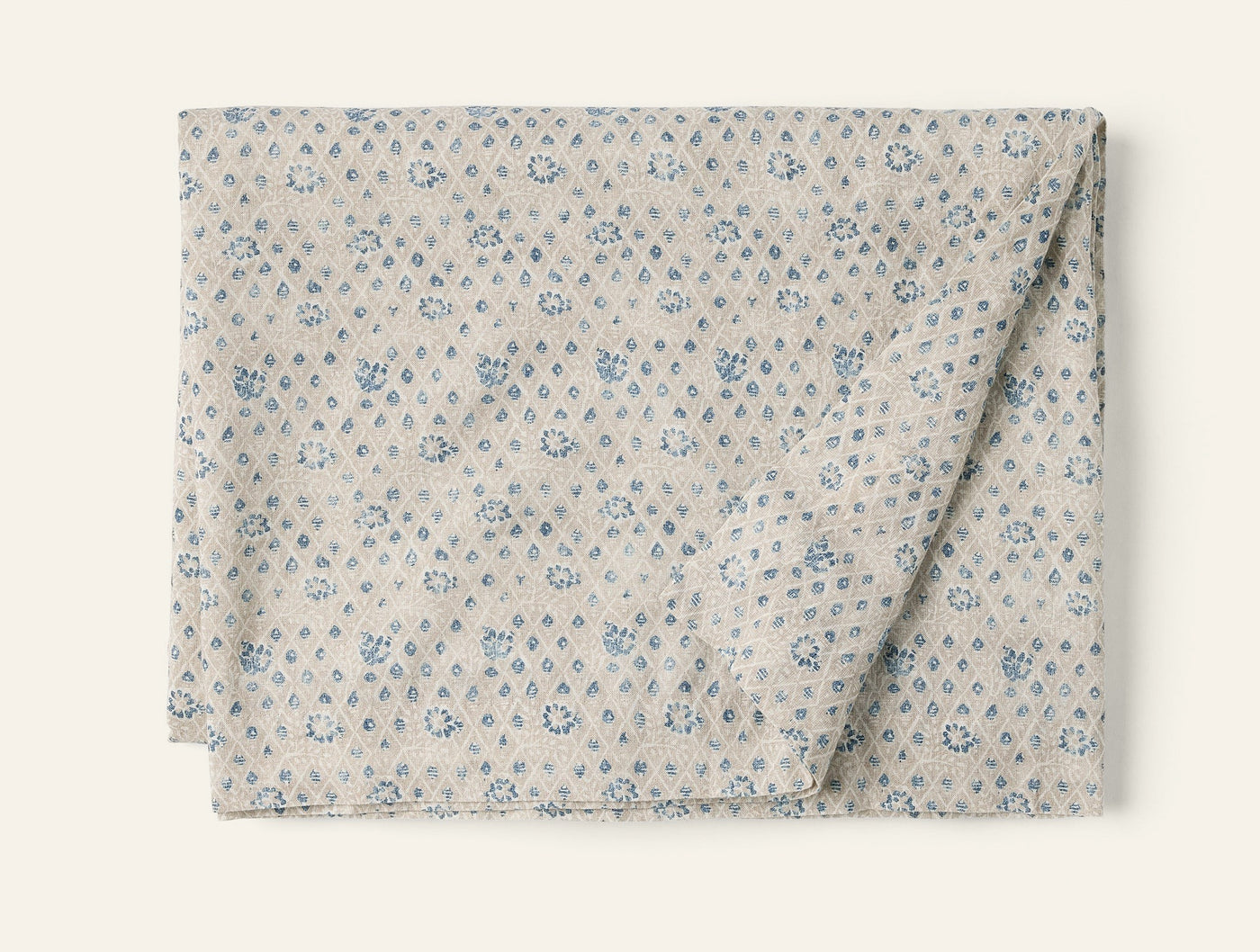 Coyuchi Coral Bell Print tablecloth, folded, oatmeal with blue floral diamond pattern.