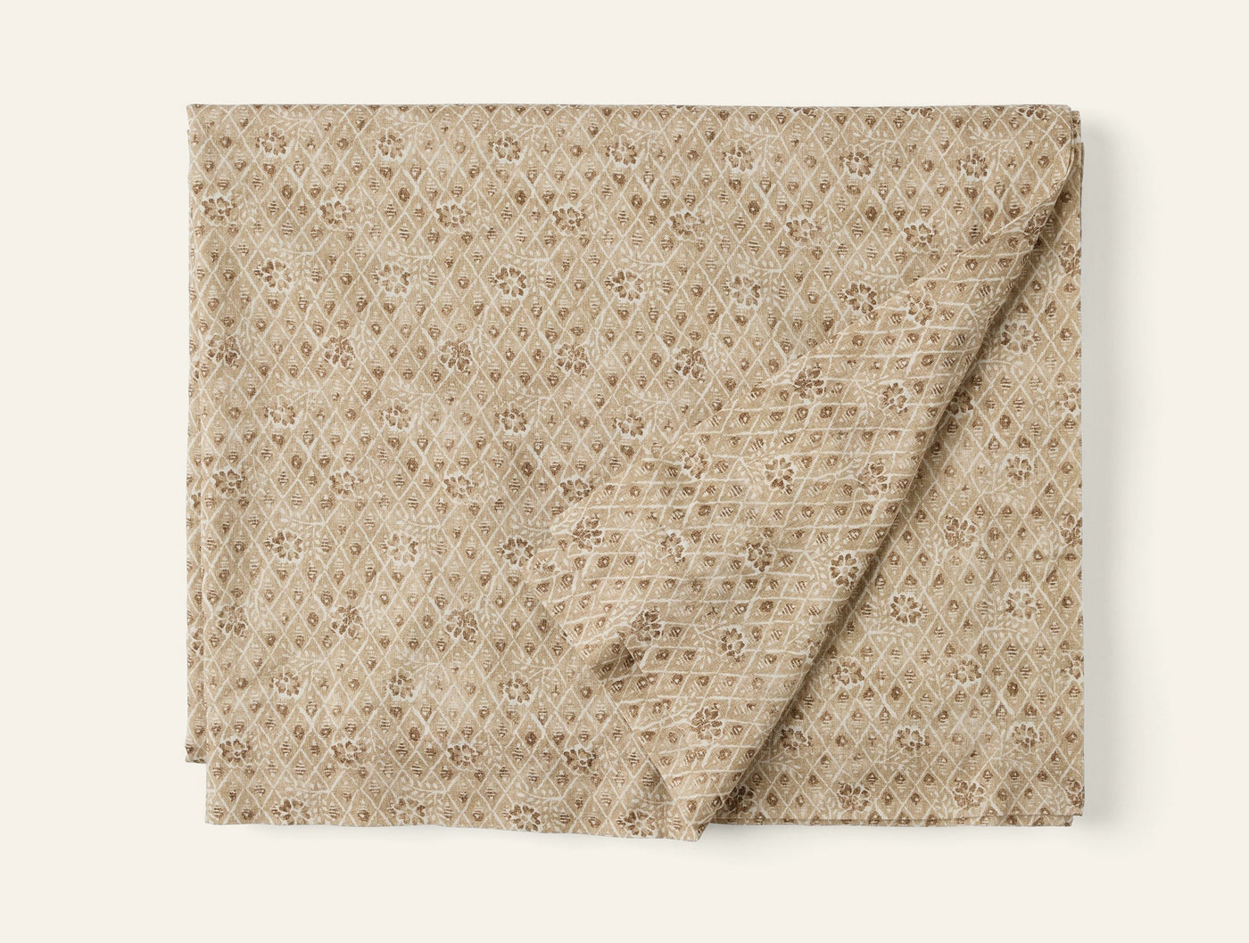 Folded sand tablecloth with allover diamond and floral block-print pattern.