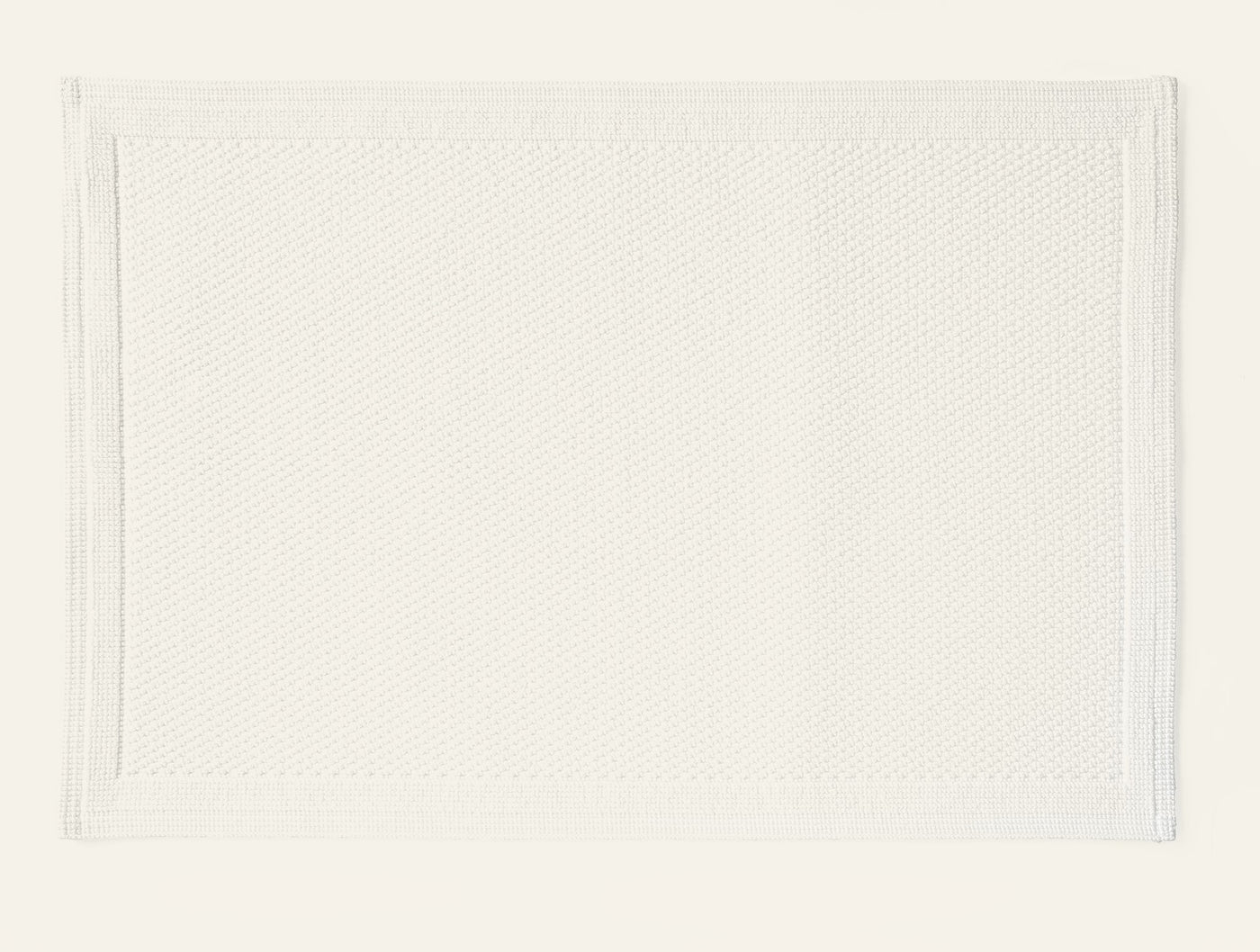 Coyuchi Cove bath rug in white with textured weave and bordered edge detail.