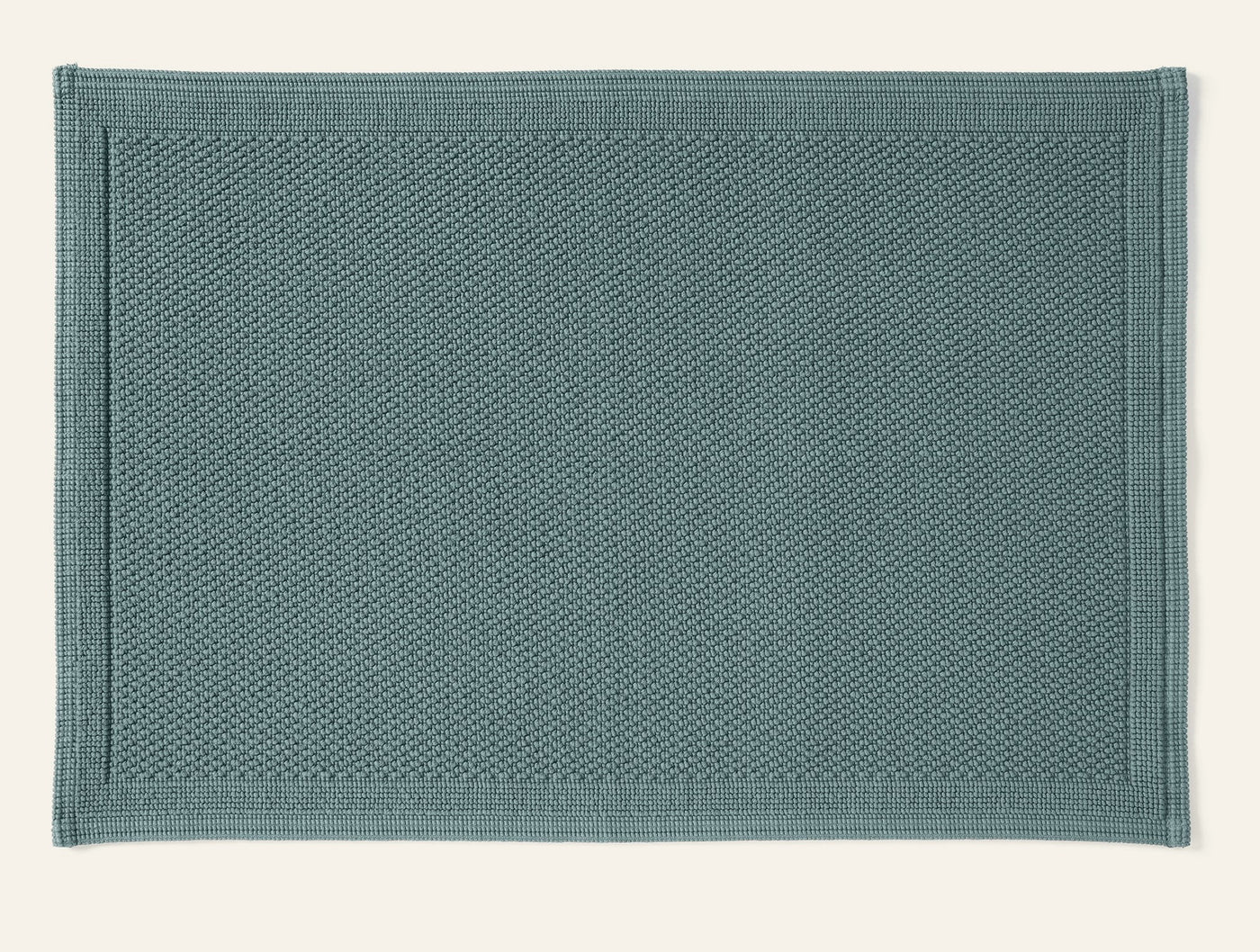 Close-up of Coyuchi Cove bath rug in slate blue, showing nubby cotton texture and border detail.