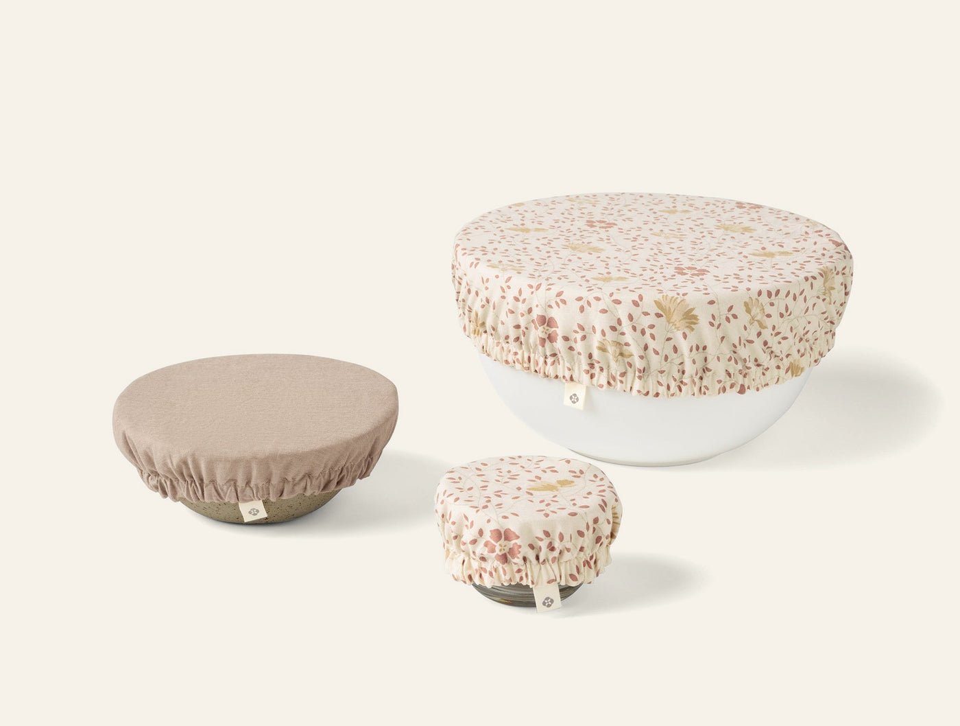 Close-up of three Coyuchi Conserve bowl covers: two floral print, one taupe, in small, medium, large sizes.