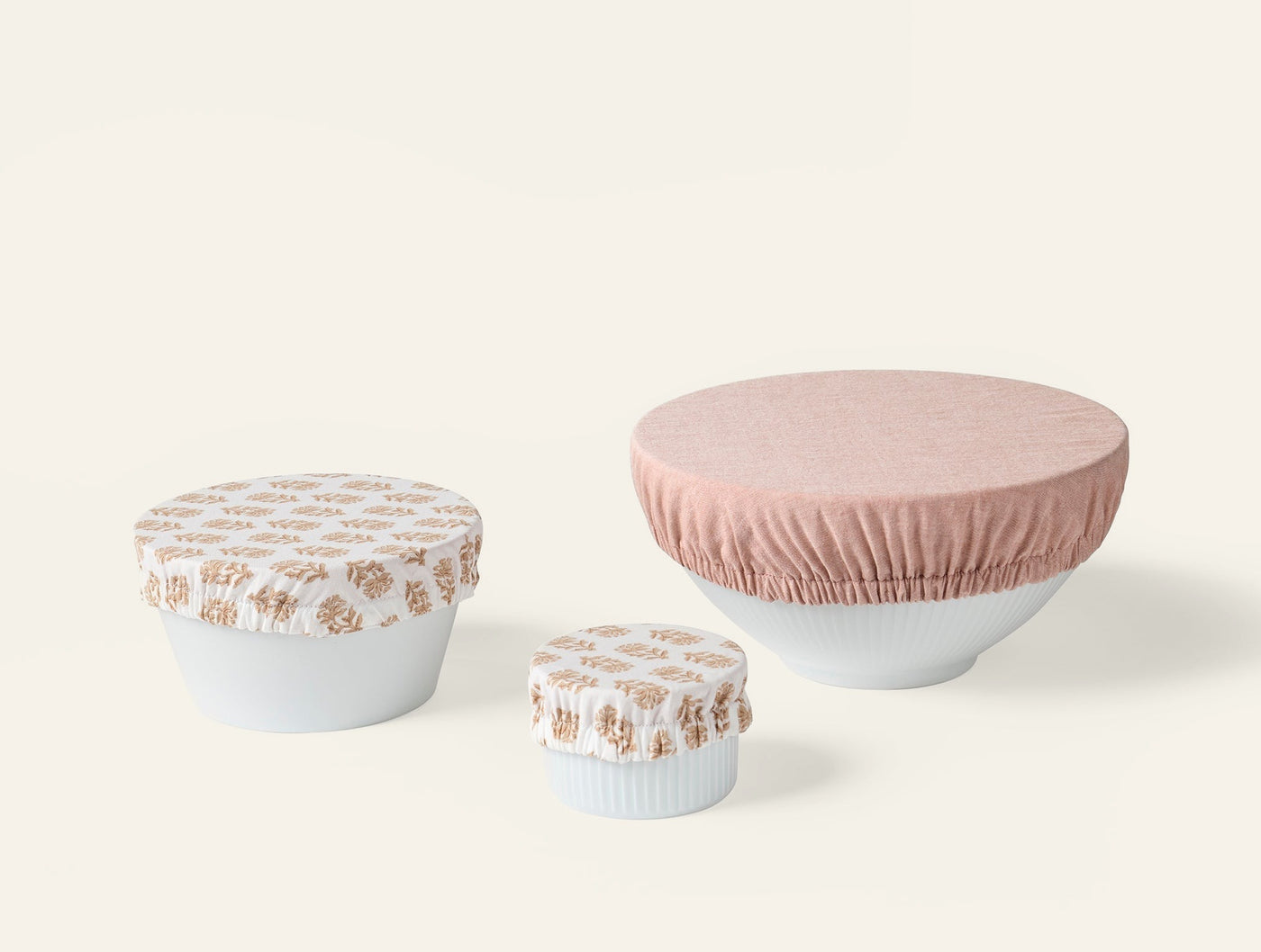 Coyuchi Conserve bowl cover set in blush and floral print, three sizes on white bowls.