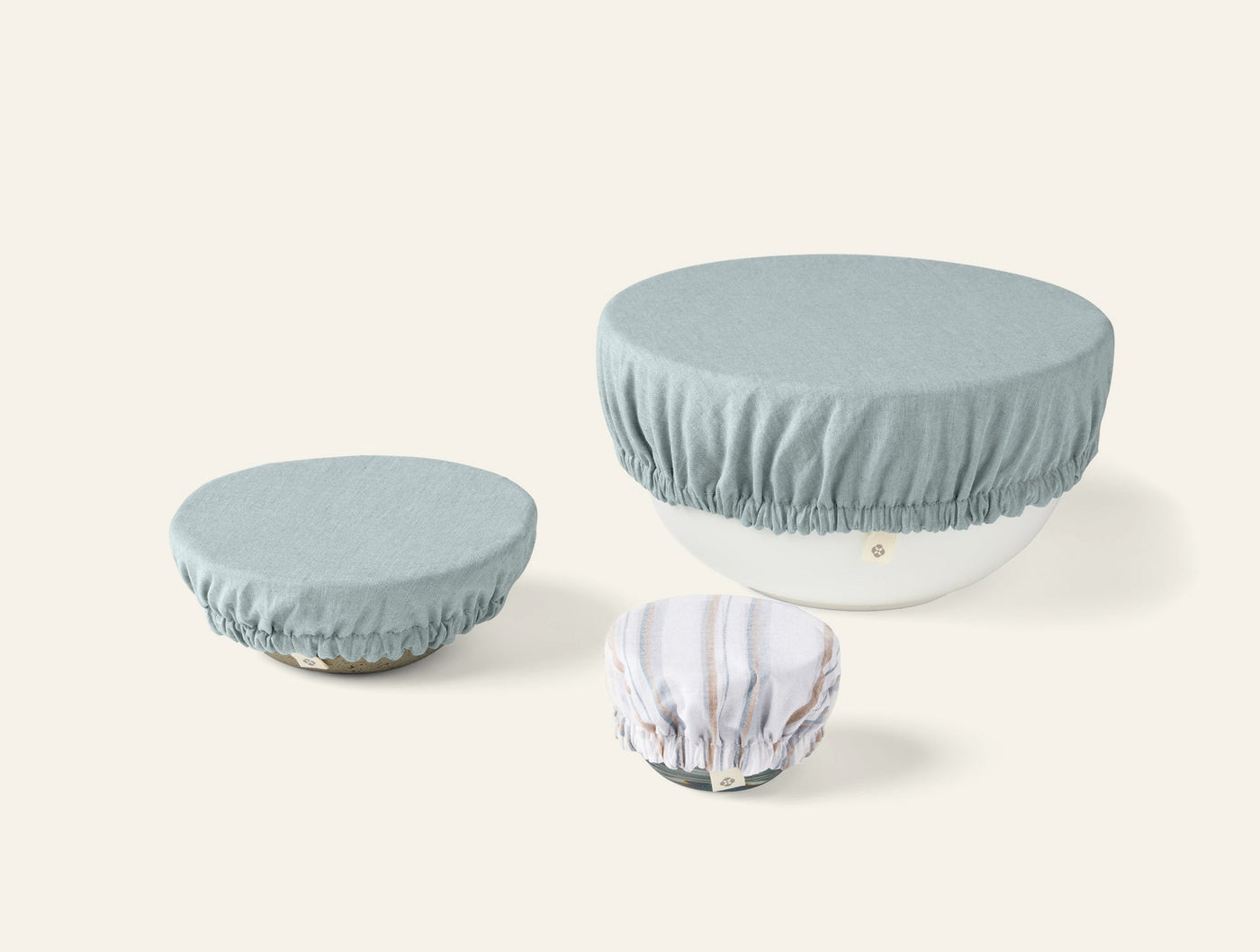 Three Coyuchi Conserve bowl covers in sage and floral print, shown in small, medium, and large sizes.
