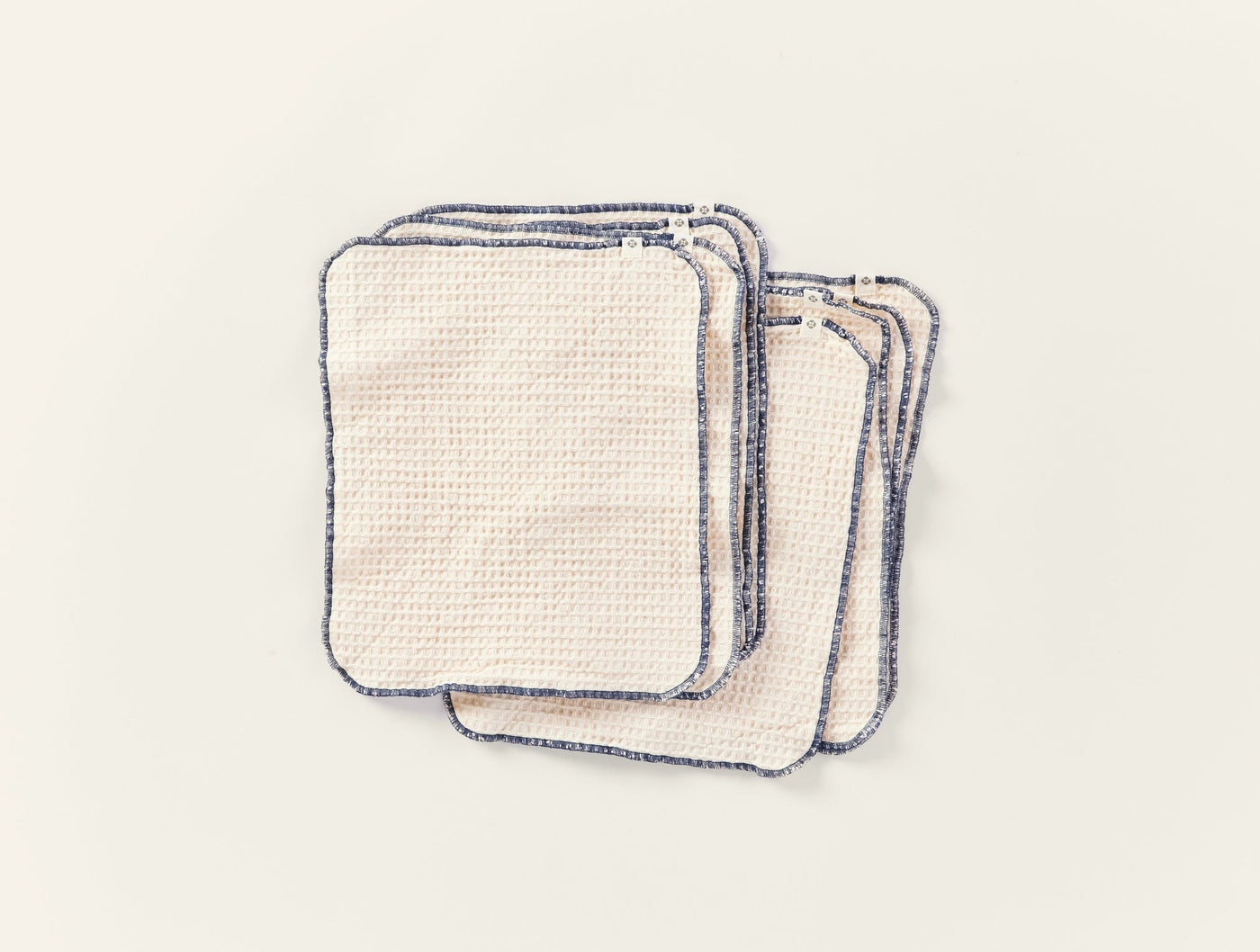 Close-up of stacked ivory Coyuchi paperless towels with navy blue contrast edge stitching.
