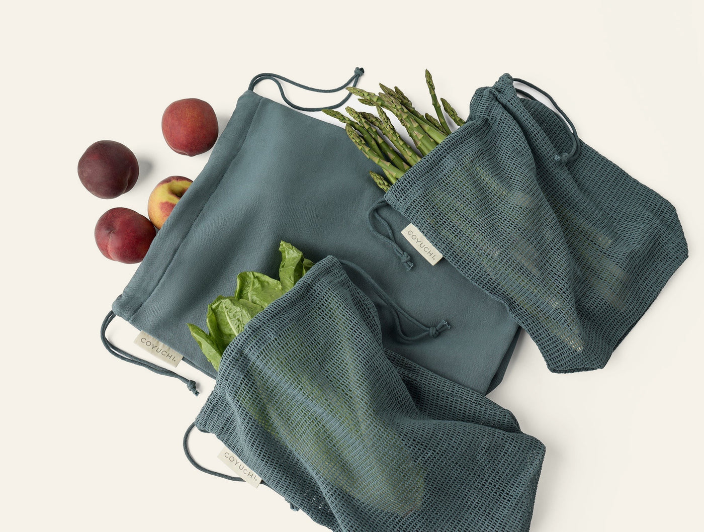 Coyuchi Conserve produce bag set in slate, styled with fresh peaches and vegetables.