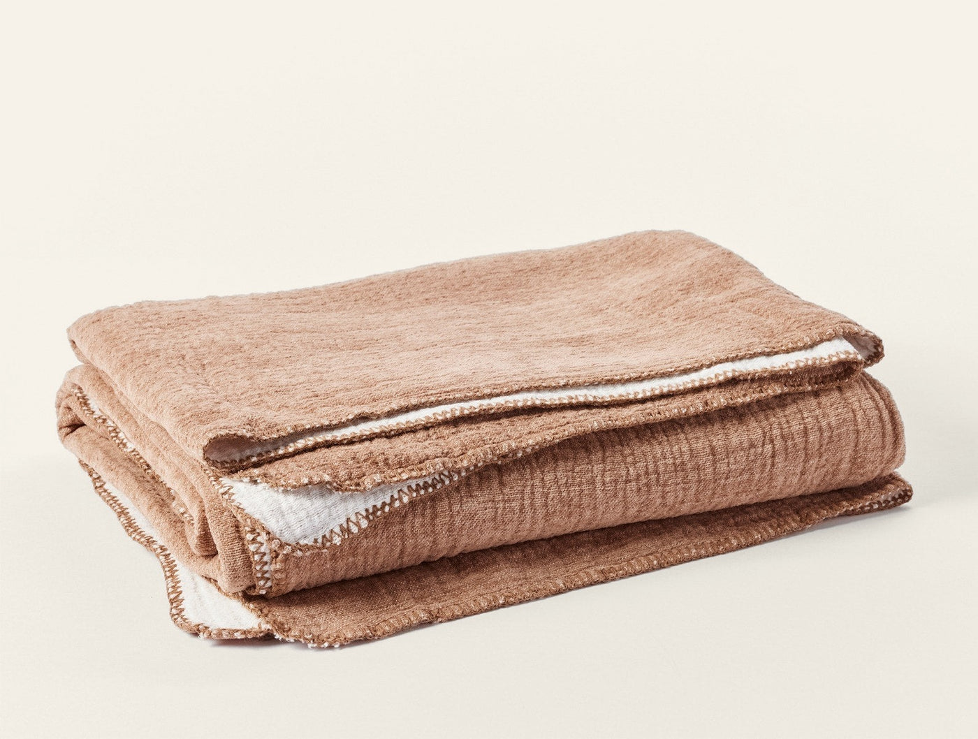 Folded camel and ivory reversible cotton blanket showing contrast lining at edges.