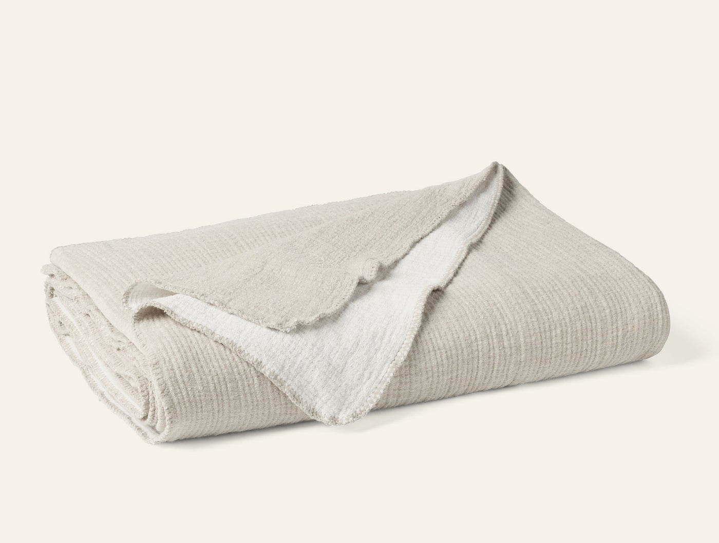 Folded ivory Coyuchi Cozy Cotton blanket showing textured weave and contrast white reverse.