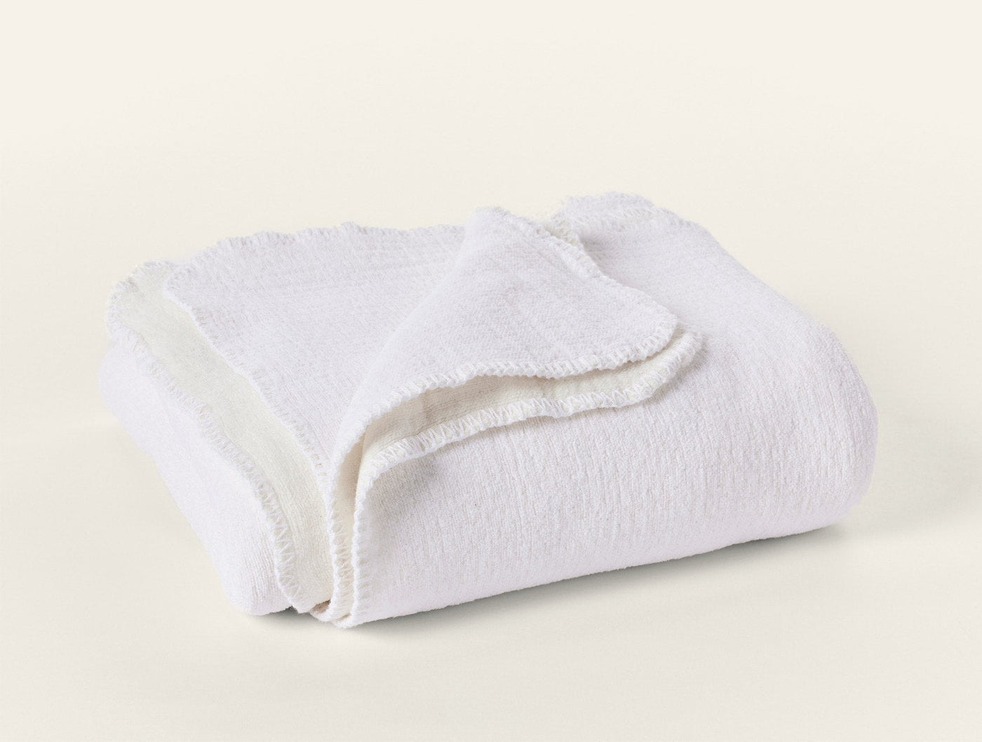 Coyuchi Cozy Cotton Throw in white, folded to show textured knit surface and scalloped trim.