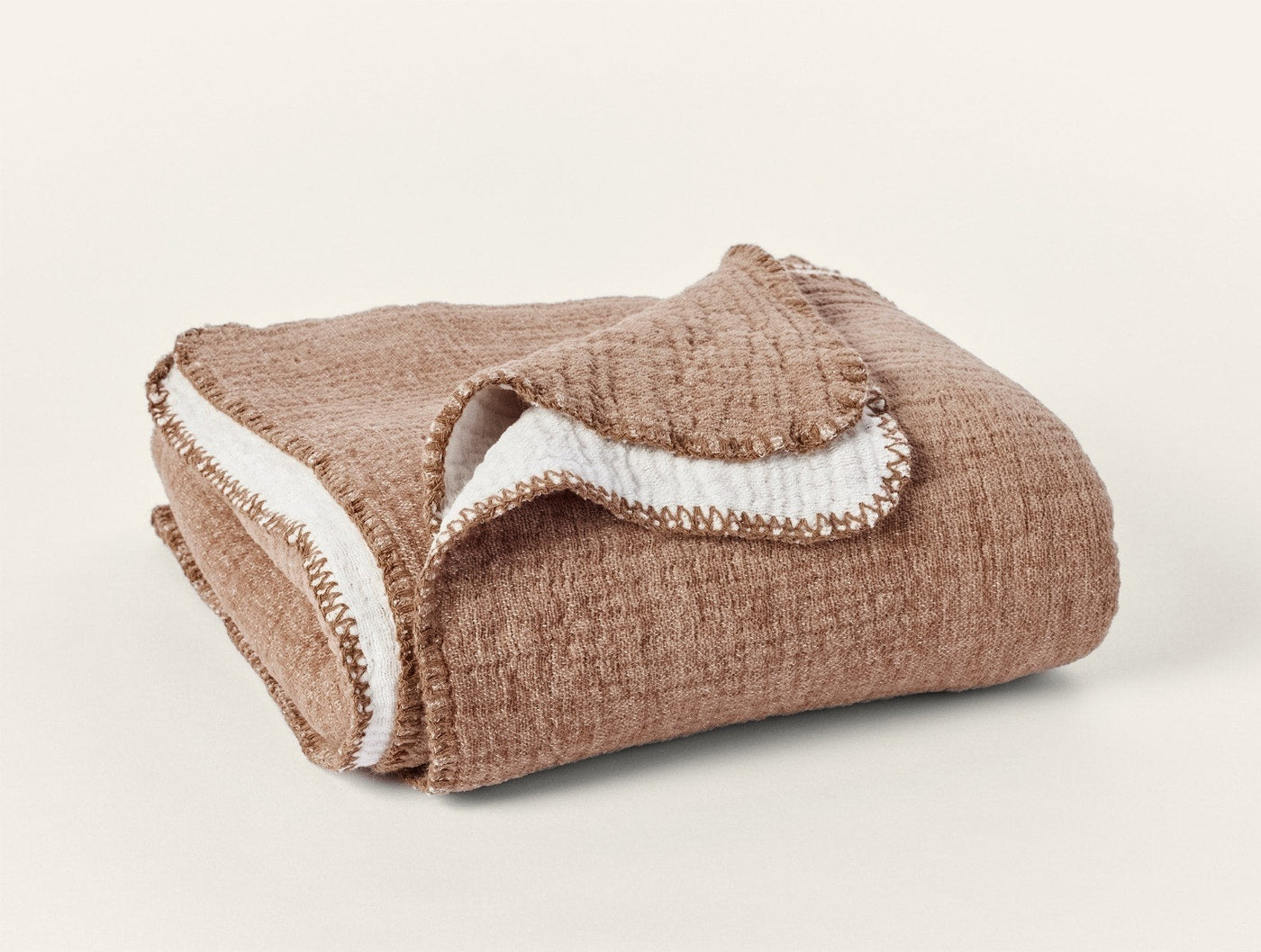Folded camel and ivory Coyuchi Cozy Cotton Throw showing blanket stitch trim detail.