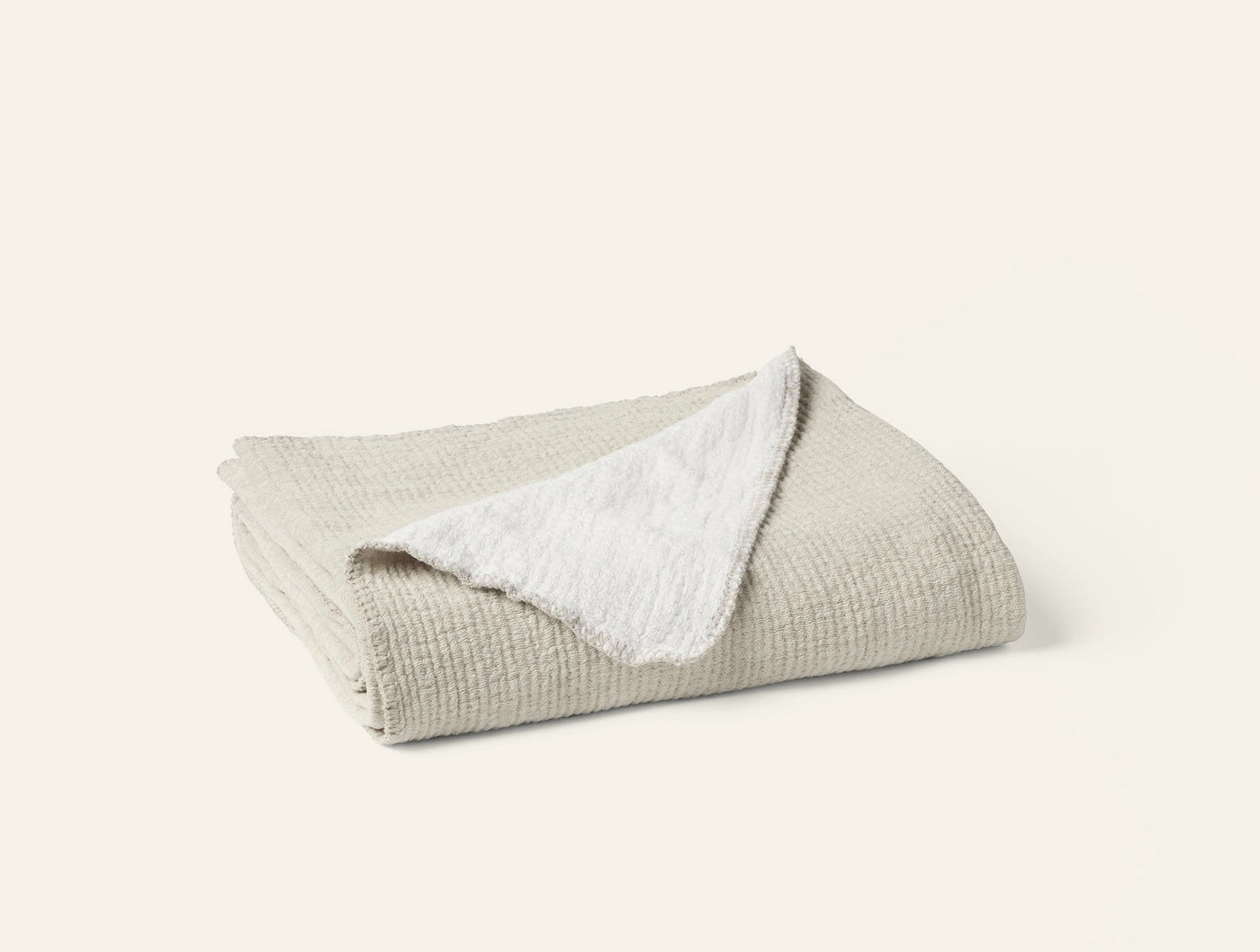 Folded Coyuchi Cozy Cotton Throw showing oatmeal waffle-textured front and white sherpa reverse.