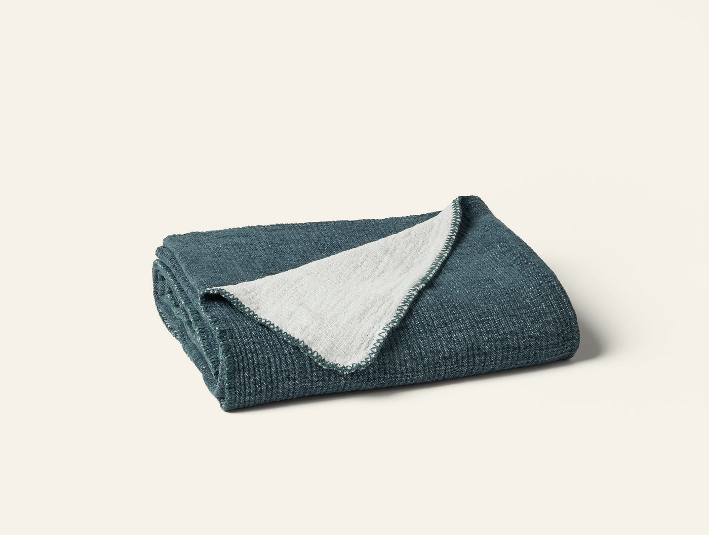 Folded teal throw with textured waffle weave exterior and ivory reverse, corner turned back.