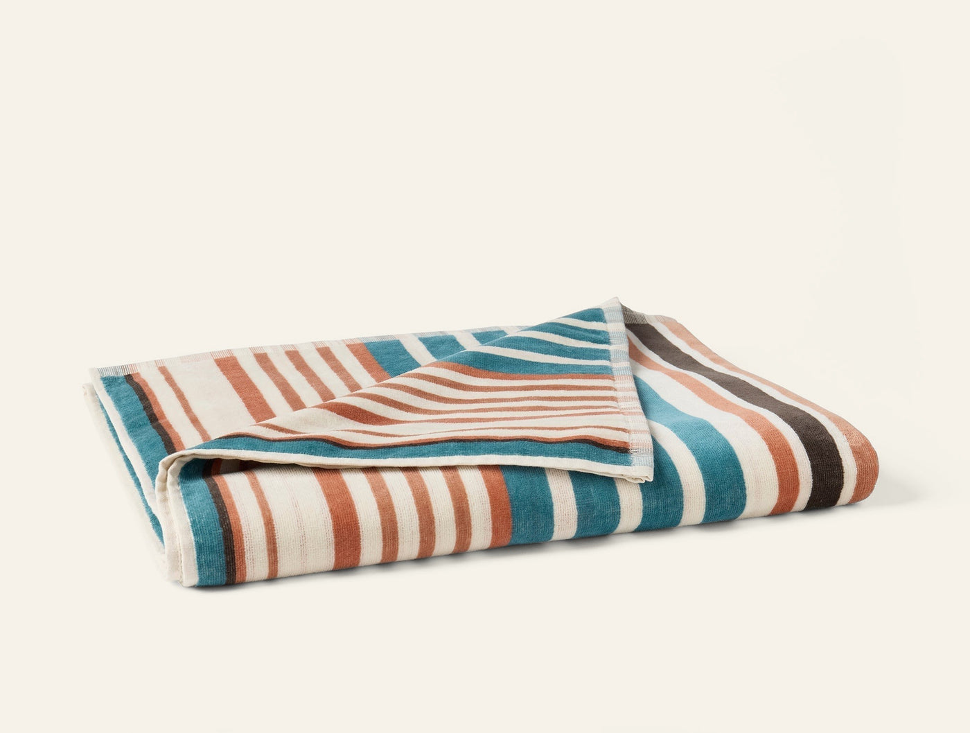 Coyuchi Dawn Stripe beach towel folded, teal, terracotta, and ivory stripes.