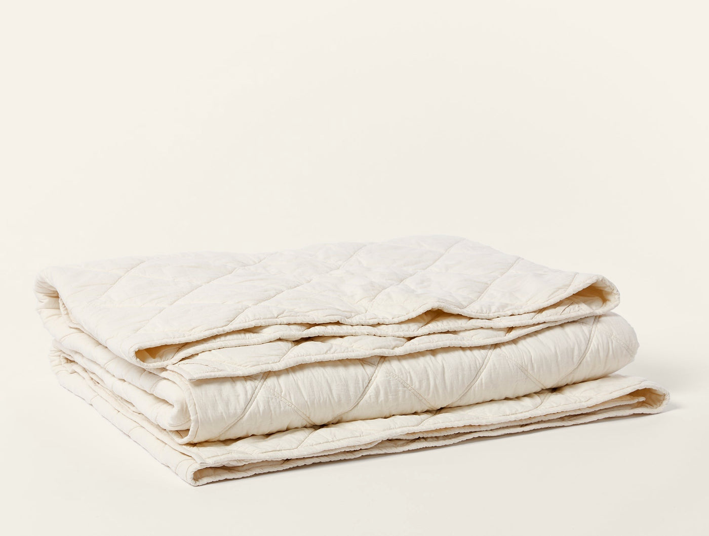 Ivory quilted comforter folded, showing diamond-stitch pattern and natural cotton texture.