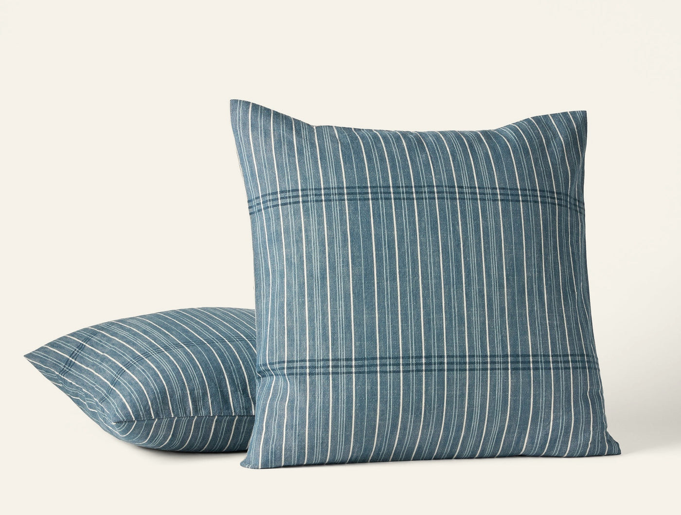 Two Coyuchi Fernwood pillows in slate blue with multi-stripe woven pattern, front and side view.