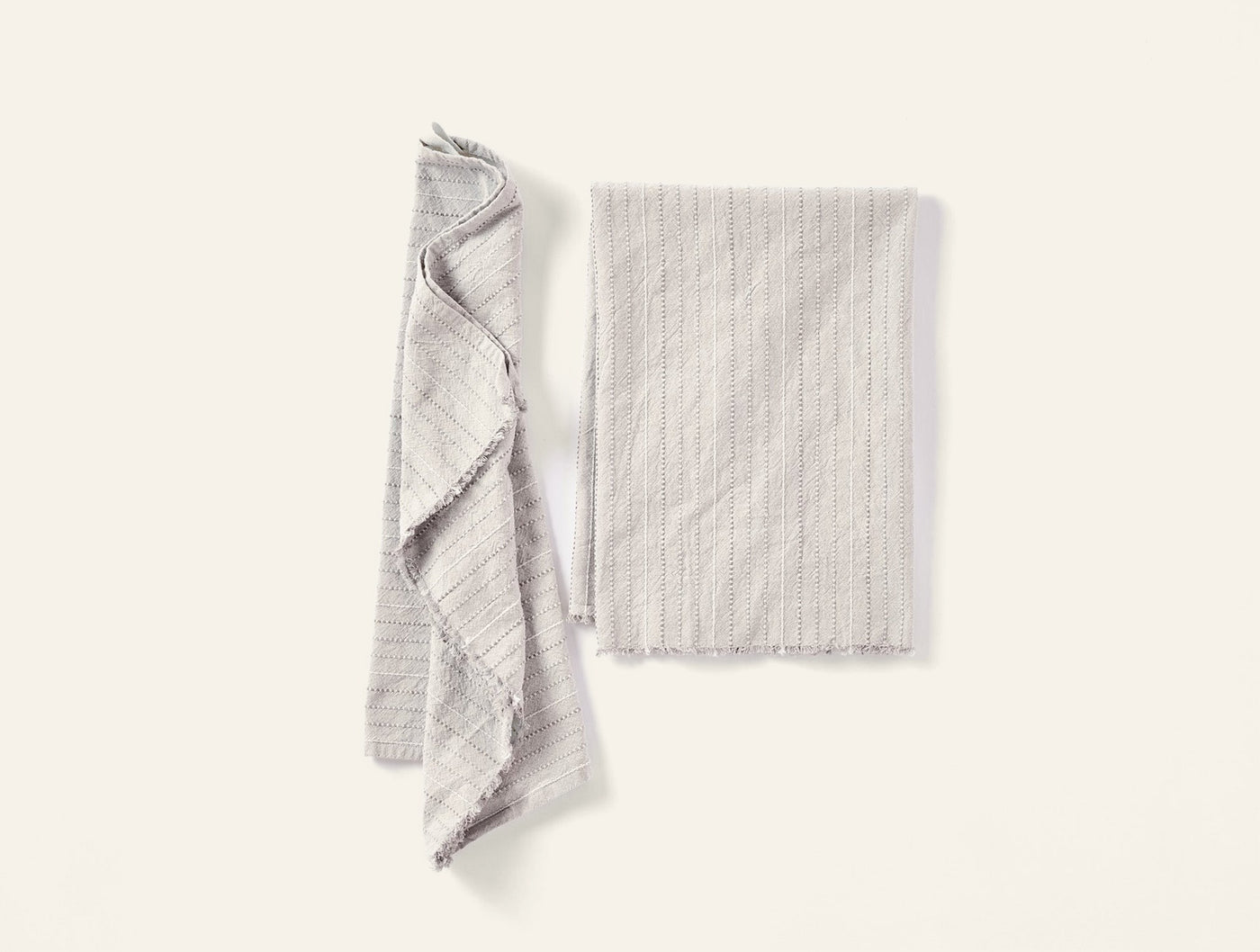 Pair of Coyuchi Fringe Stripe hand towels in natural, one folded, one draped.